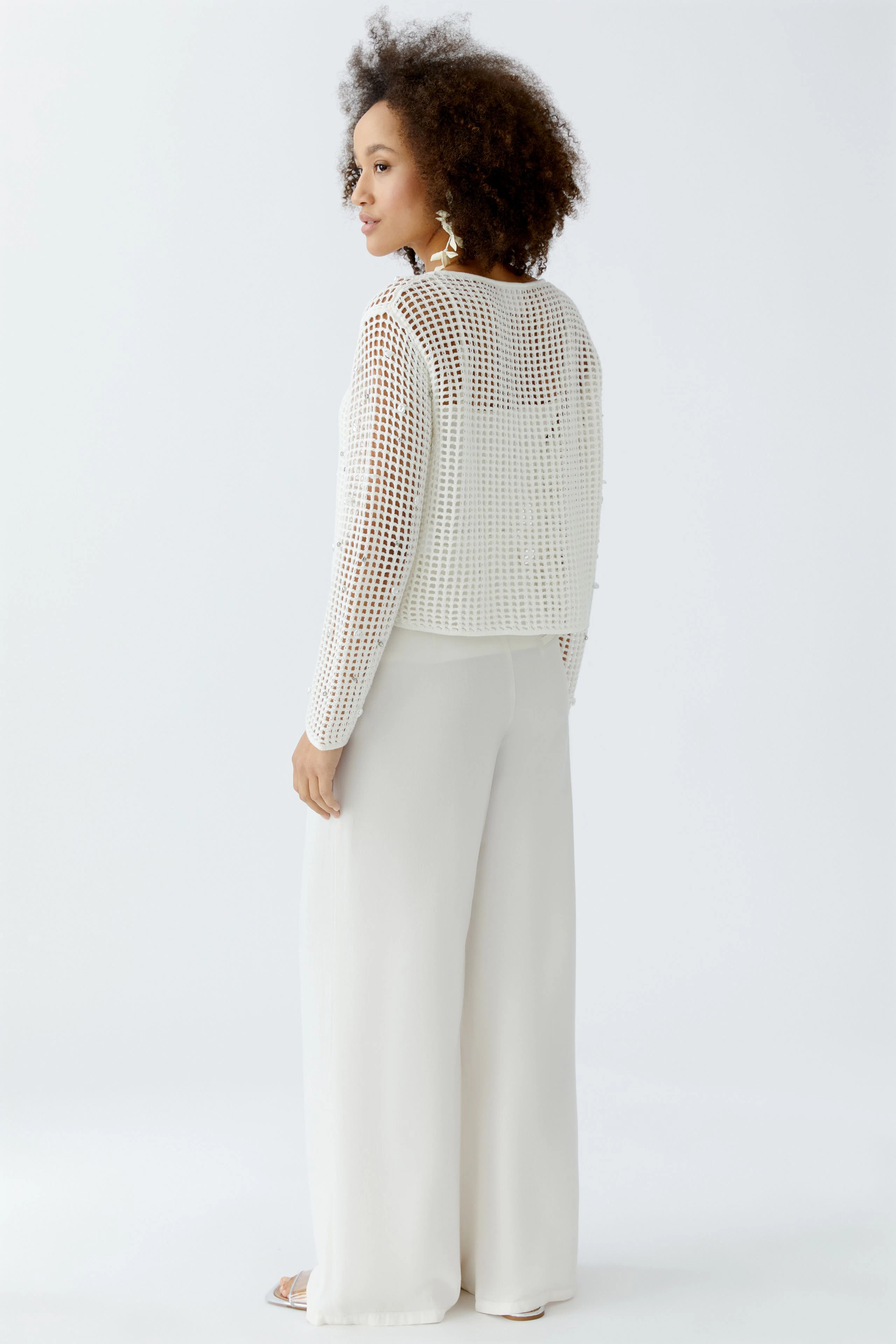 Modern women's pullover: A woman in a white, cropped pullover with a mesh design, paired with wide trousers.