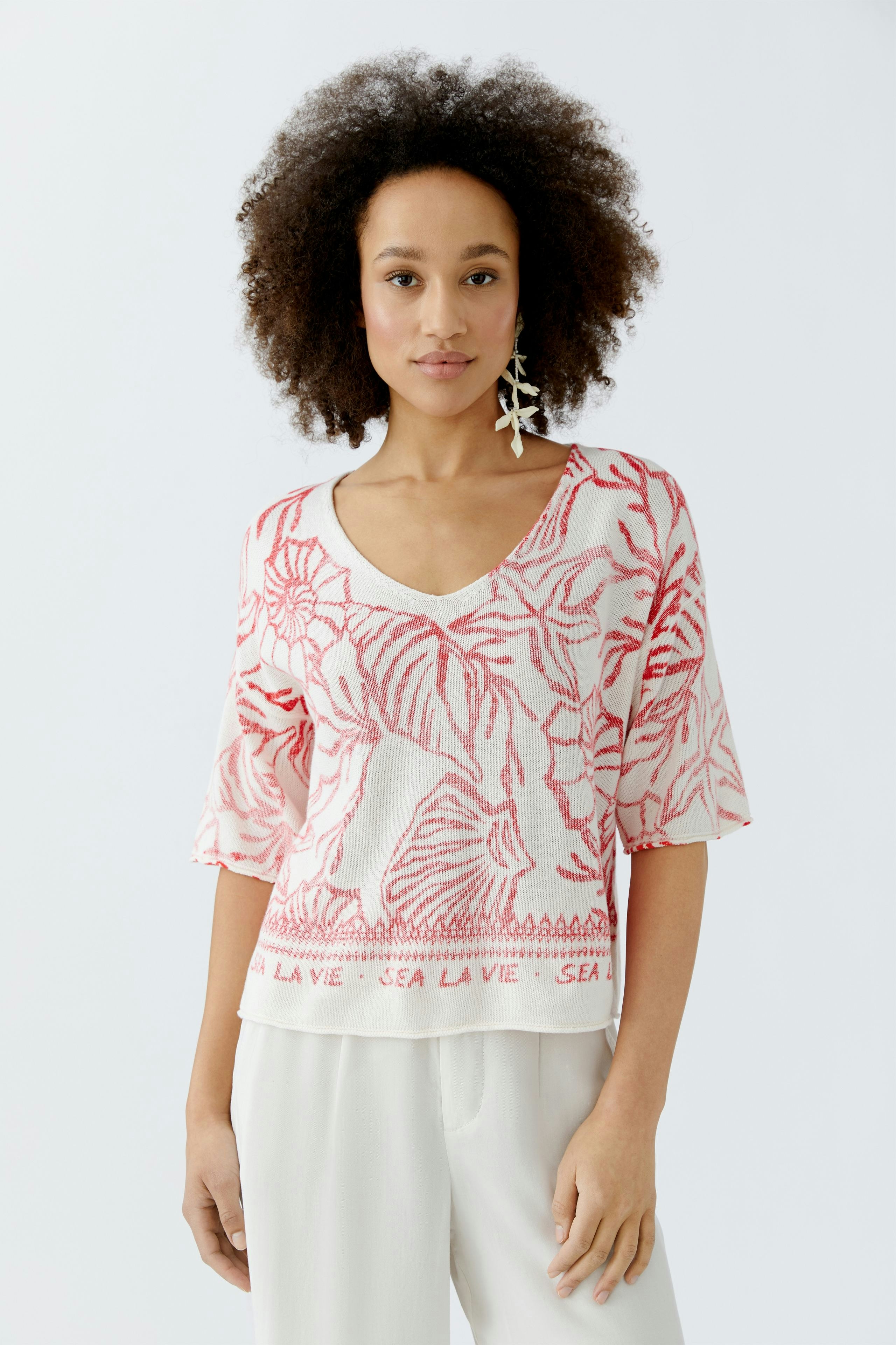 Damen-Pullover: Frau trägt einen lässigen, rosa Pullover mit floralem Muster und V-Ausschnitt.