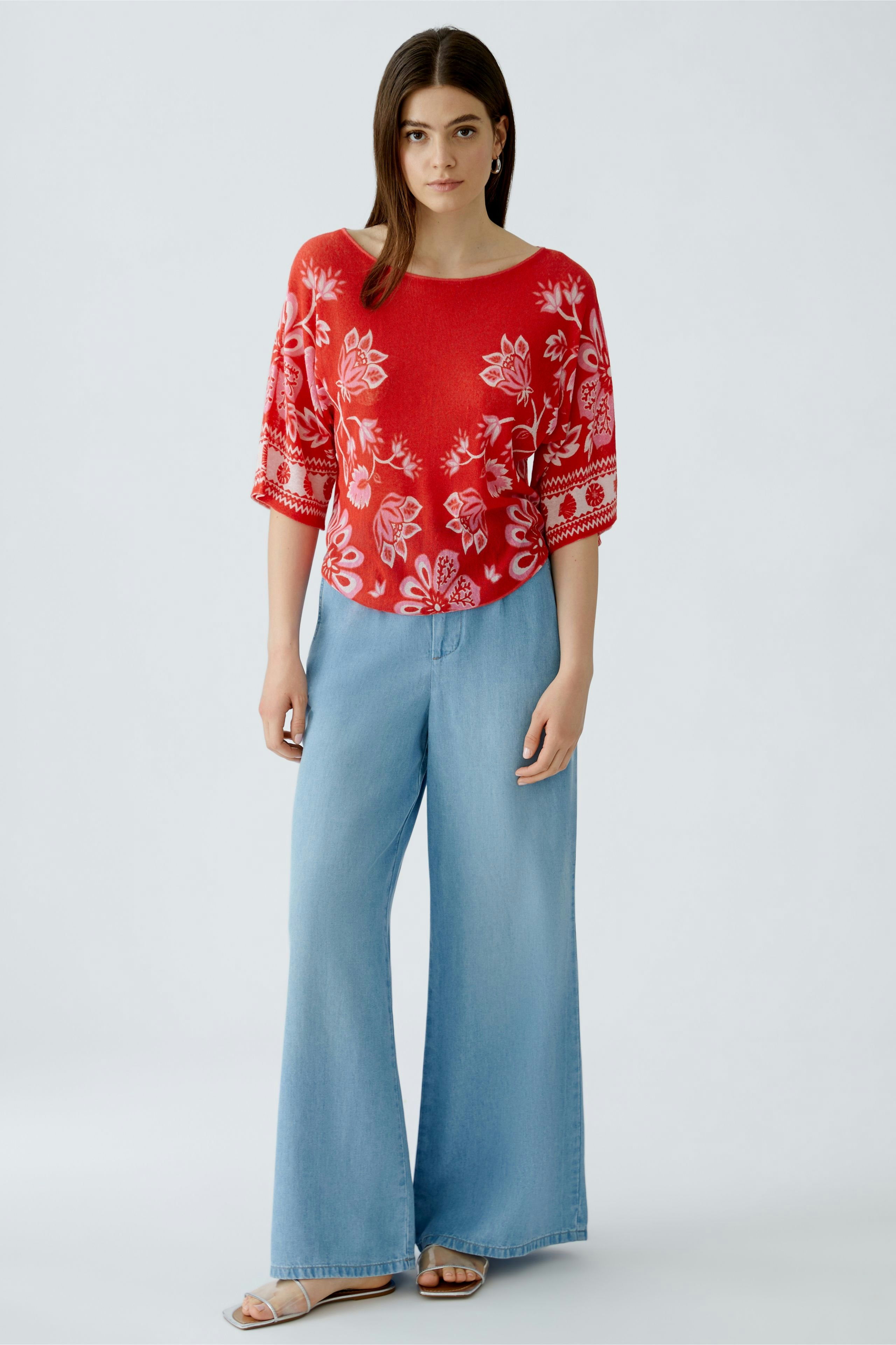 Casual women's pullover: Young woman in a red floral pullover paired with wide-leg jeans.