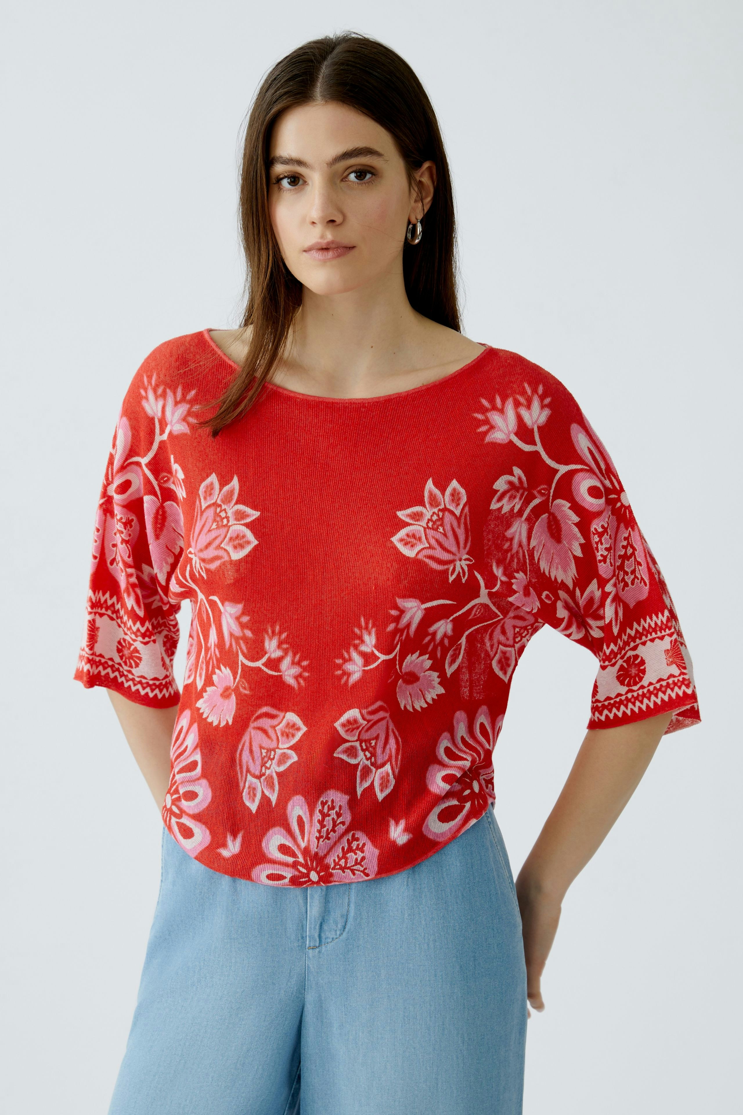 Casual women's pullover: A woman in a red floral pullover paired with light blue jeans.