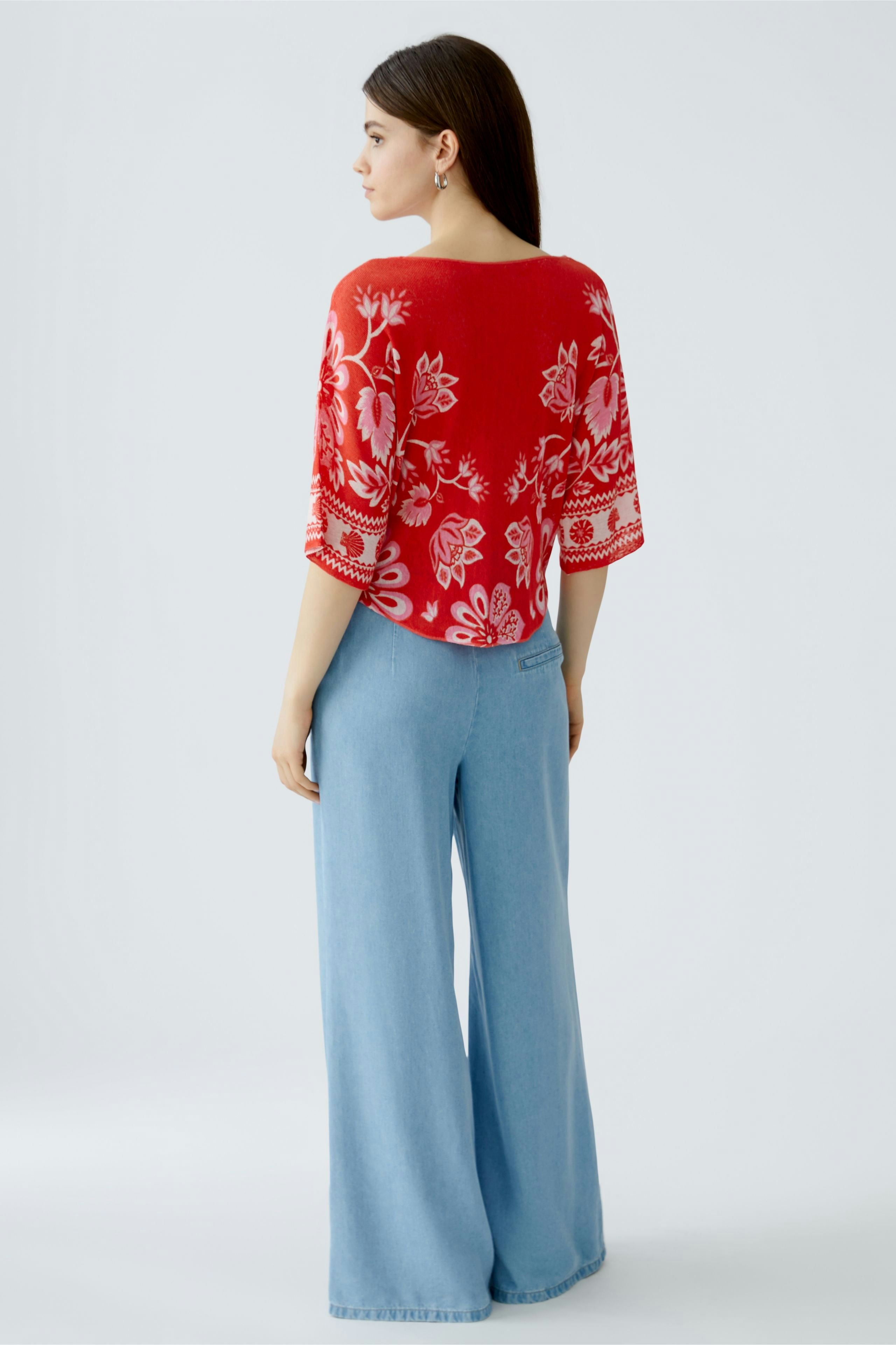 Casual women's pullover: A woman in a red floral pullover paired with light blue wide-leg jeans.