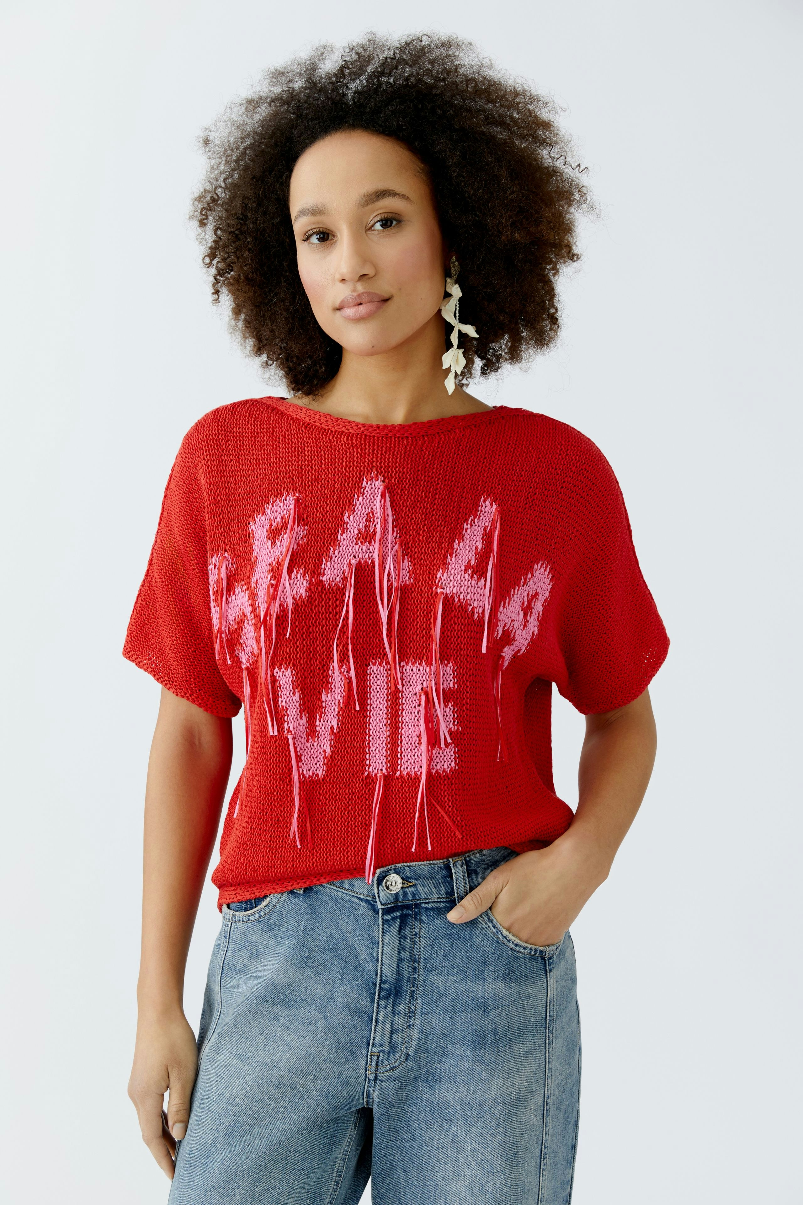 Casual women's pullover: Young woman in a red knit pullover with bold lettering, paired with relaxed jeans.