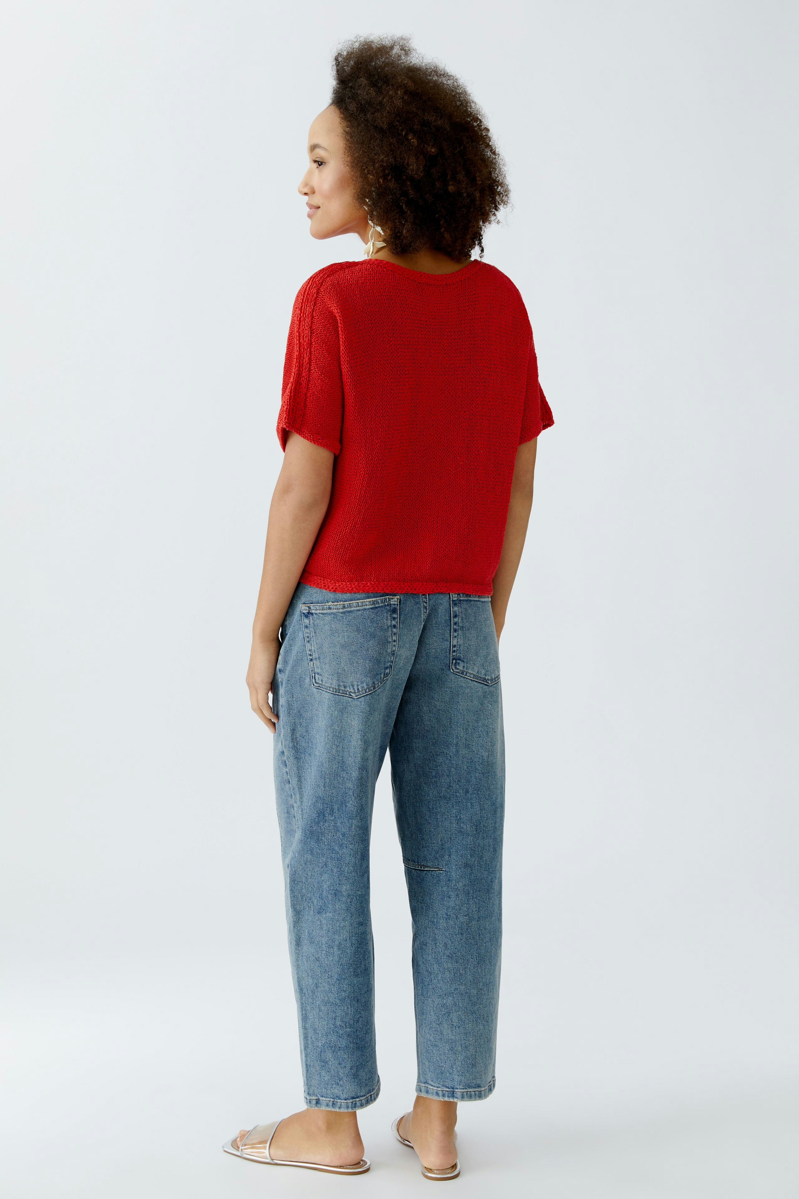 Casual women's pullover: Young woman in a red knitted pullover with short sleeves and relaxed jeans.