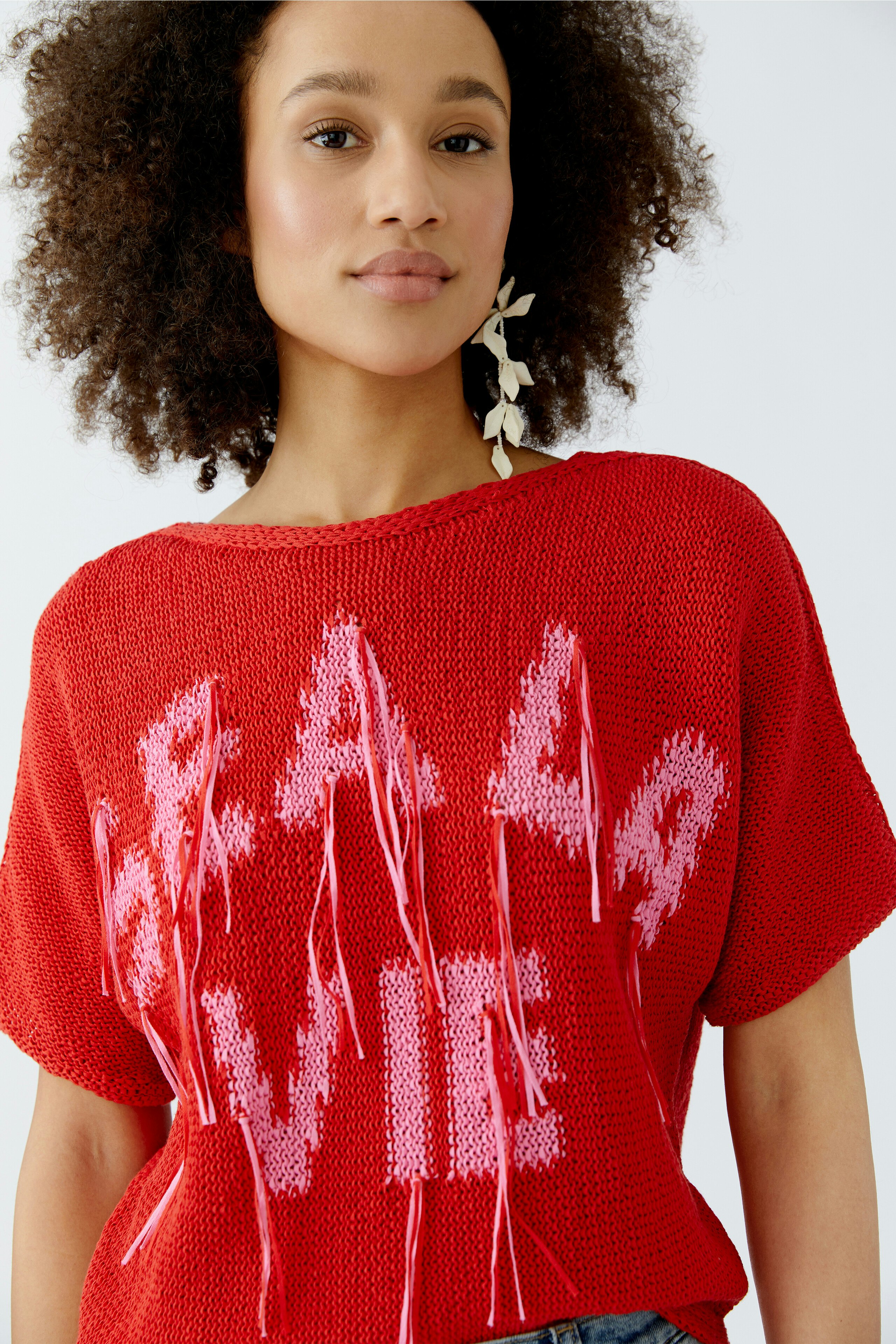 Casual women's pullover: Young woman in a red knit pullover with playful lettering and fringes.