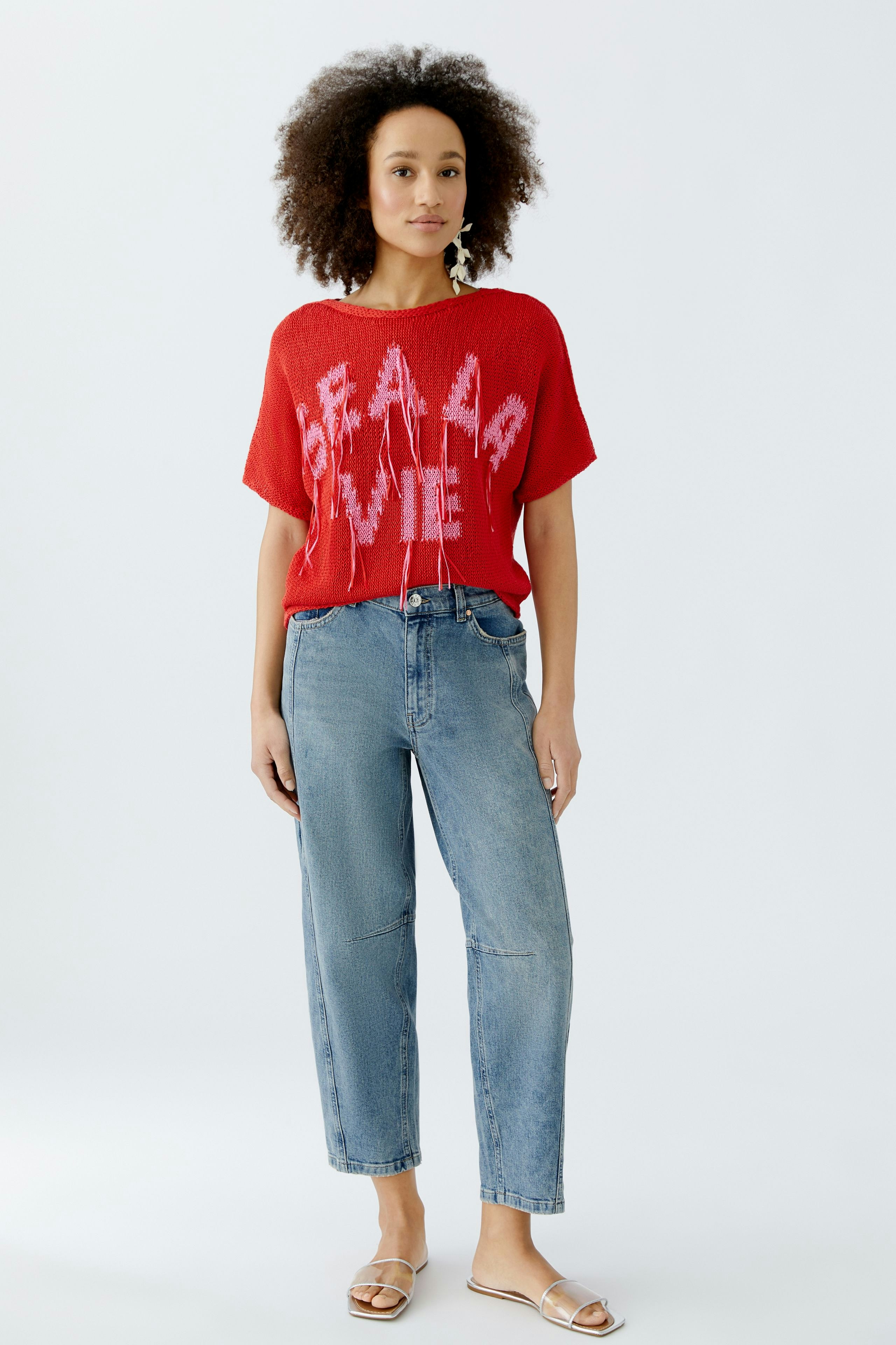 Casual women's pullover: Young woman in a red knit pullover with bold lettering and relaxed jeans.