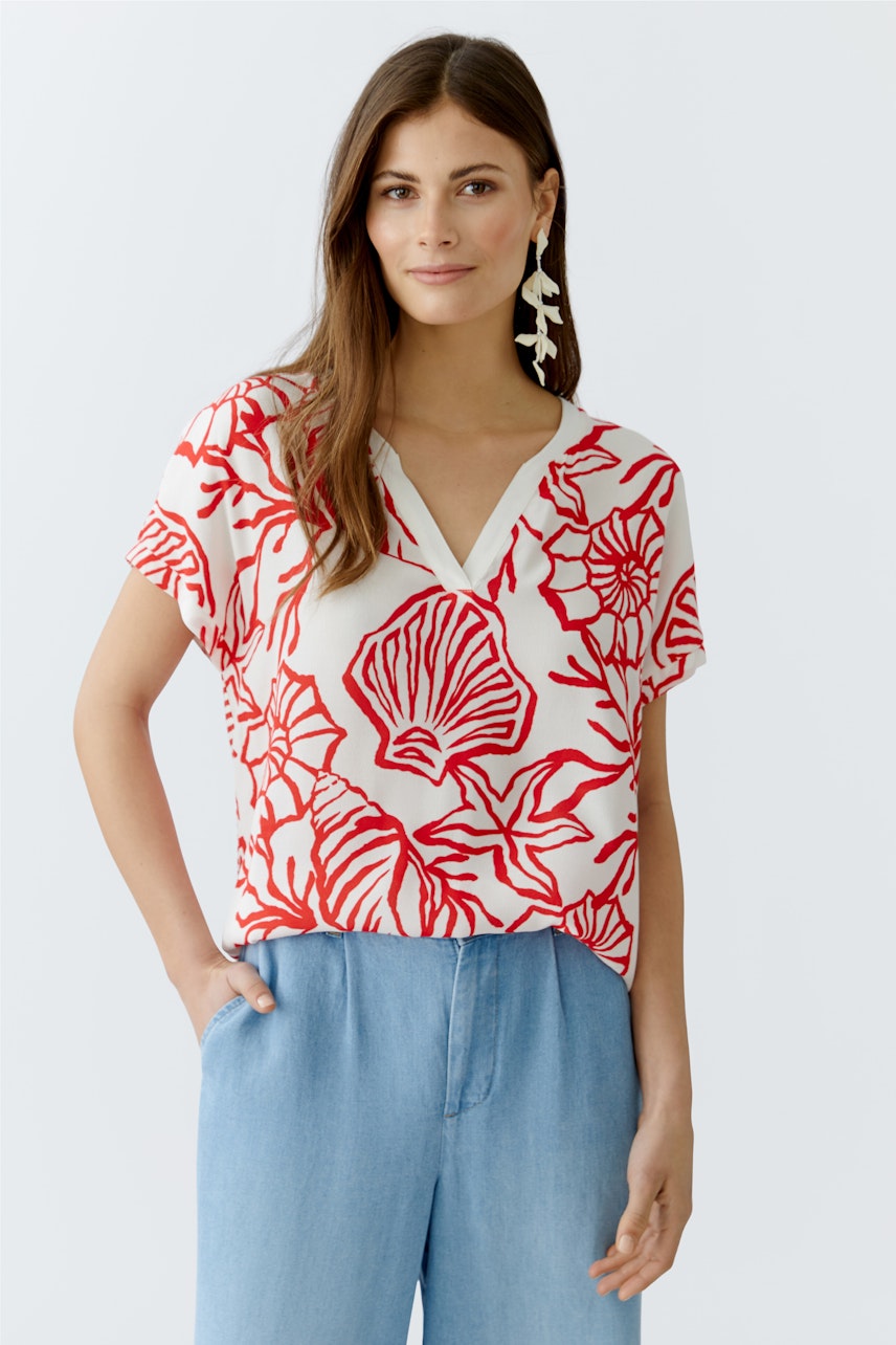 Blusenshirt: Frau trägt ein rotes, floral gemustertes Blusenshirt mit V-Ausschnitt und lässiger Passform.
