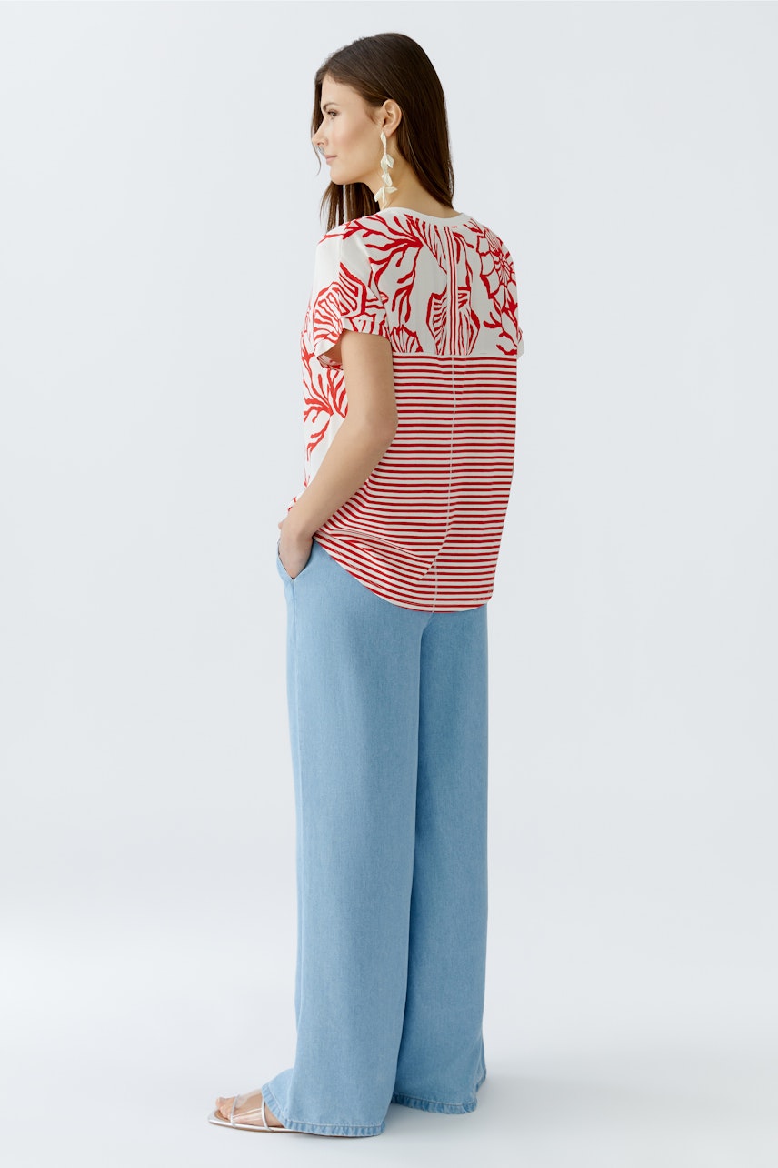 Blusenshirt: Frau trägt ein gestreiftes Shirt mit floralem Muster und lockeren Jeans.