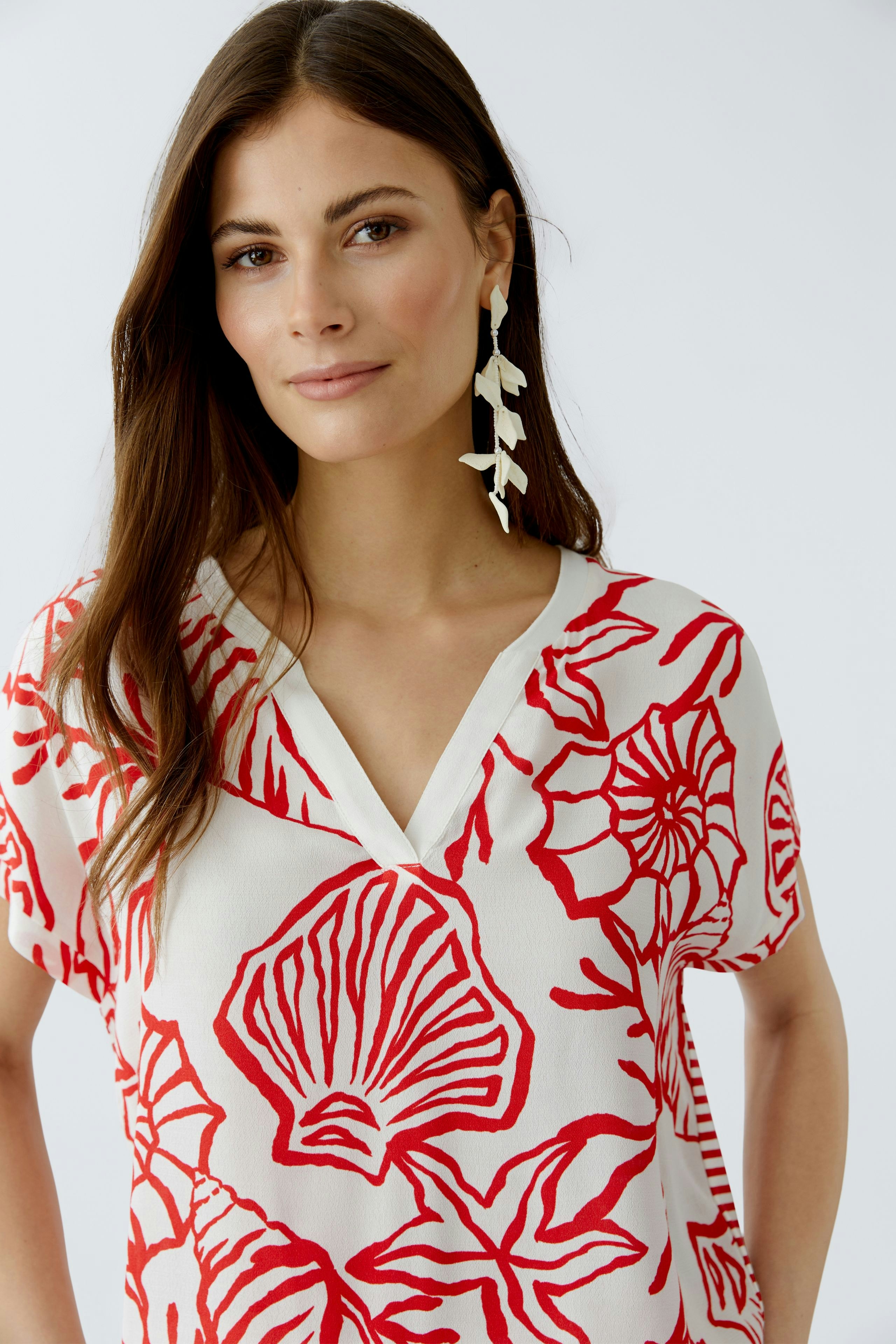 Casual women's blouse shirt: A woman in a white top with red floral patterns, featuring a V-neck design.