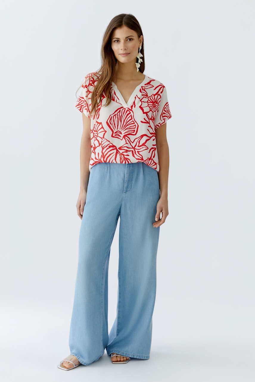Luftiges Blusenshirt: Frau trägt ein rotes Shirt mit floralem Muster und weiten Jeans, lässiger Look.