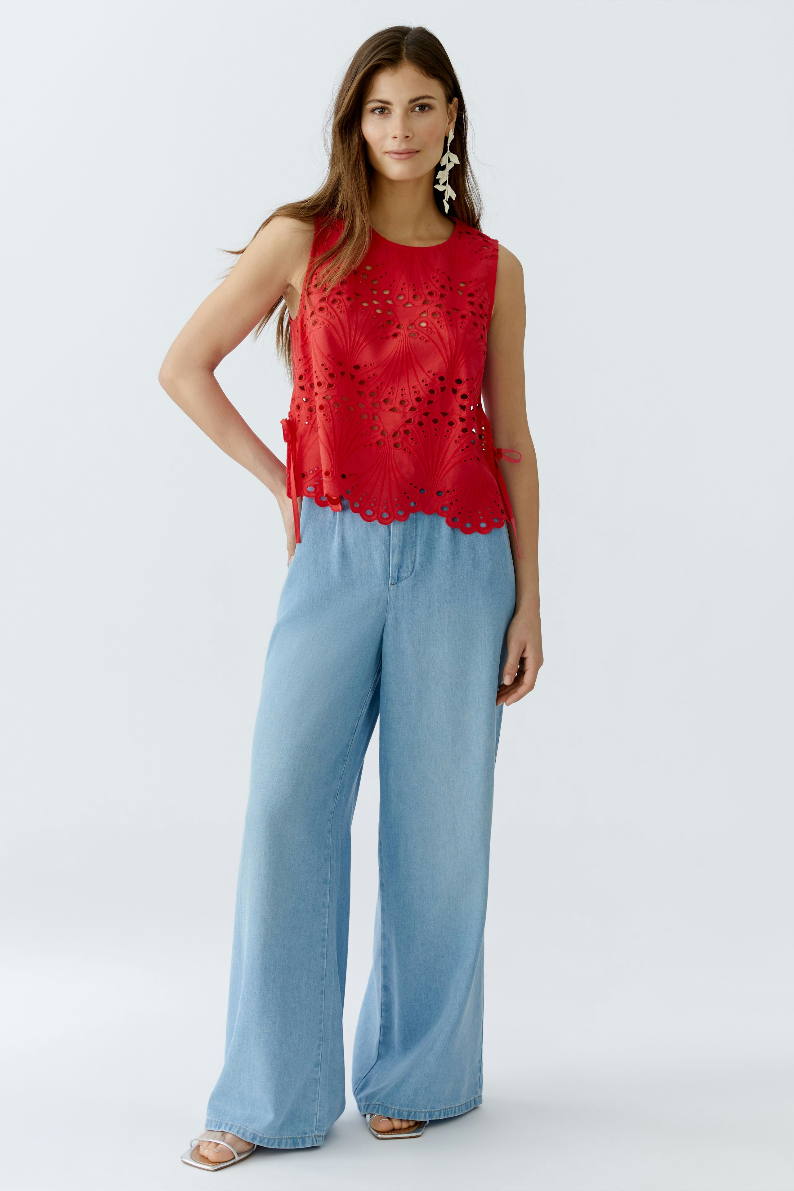 Casual women's top: A woman in a red sleeveless top with cut-out details and light blue wide-leg jeans.