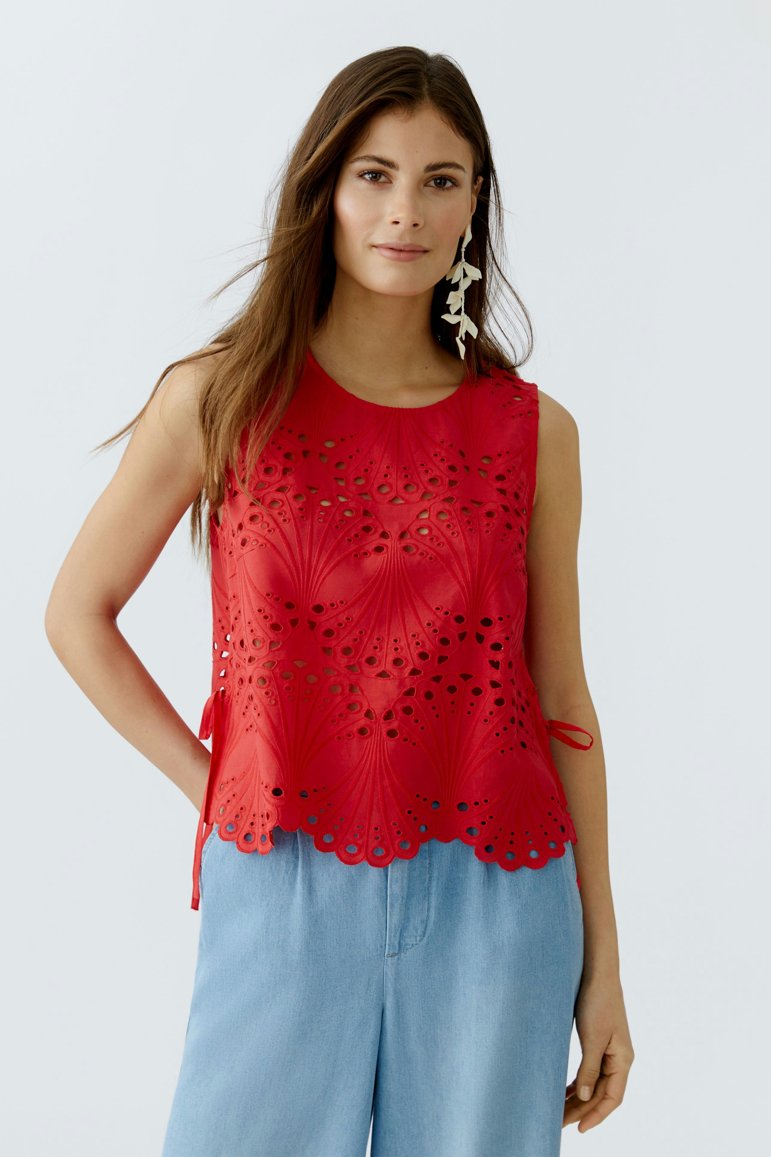 Casual women's top: A woman in a red sleeveless top with cut-out details, paired with light blue pants.