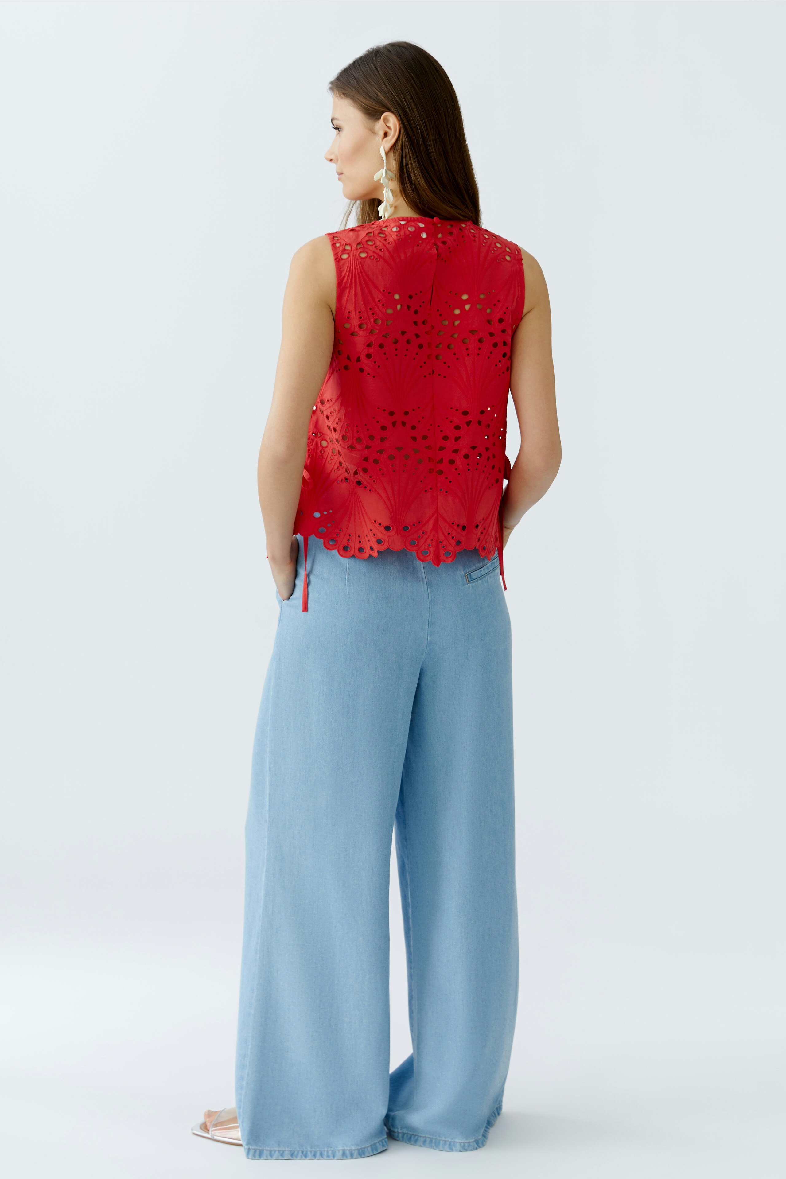 Casual women's top: A woman in a red sleeveless top with cut-out details and light blue wide-leg pants.