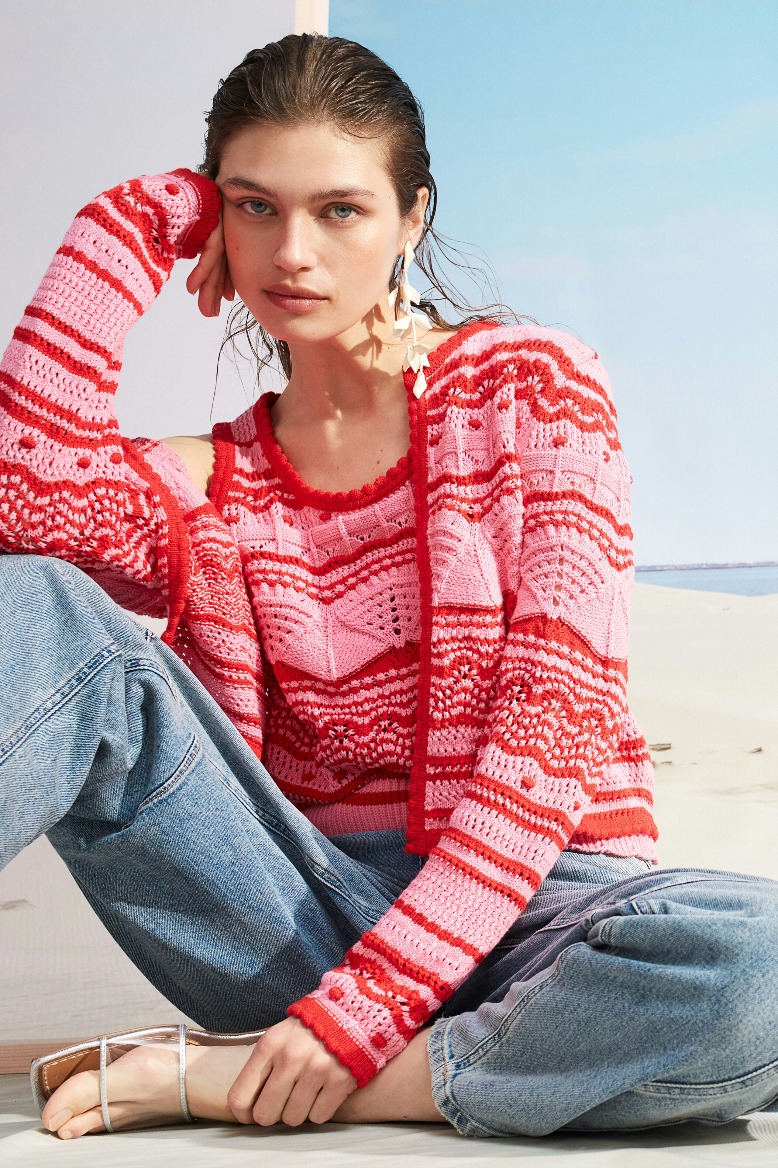 Feminines Damen-Top: Junge Frau in einem bunten, gestrickten Top mit langen Ärmeln und lässigen Jeans.