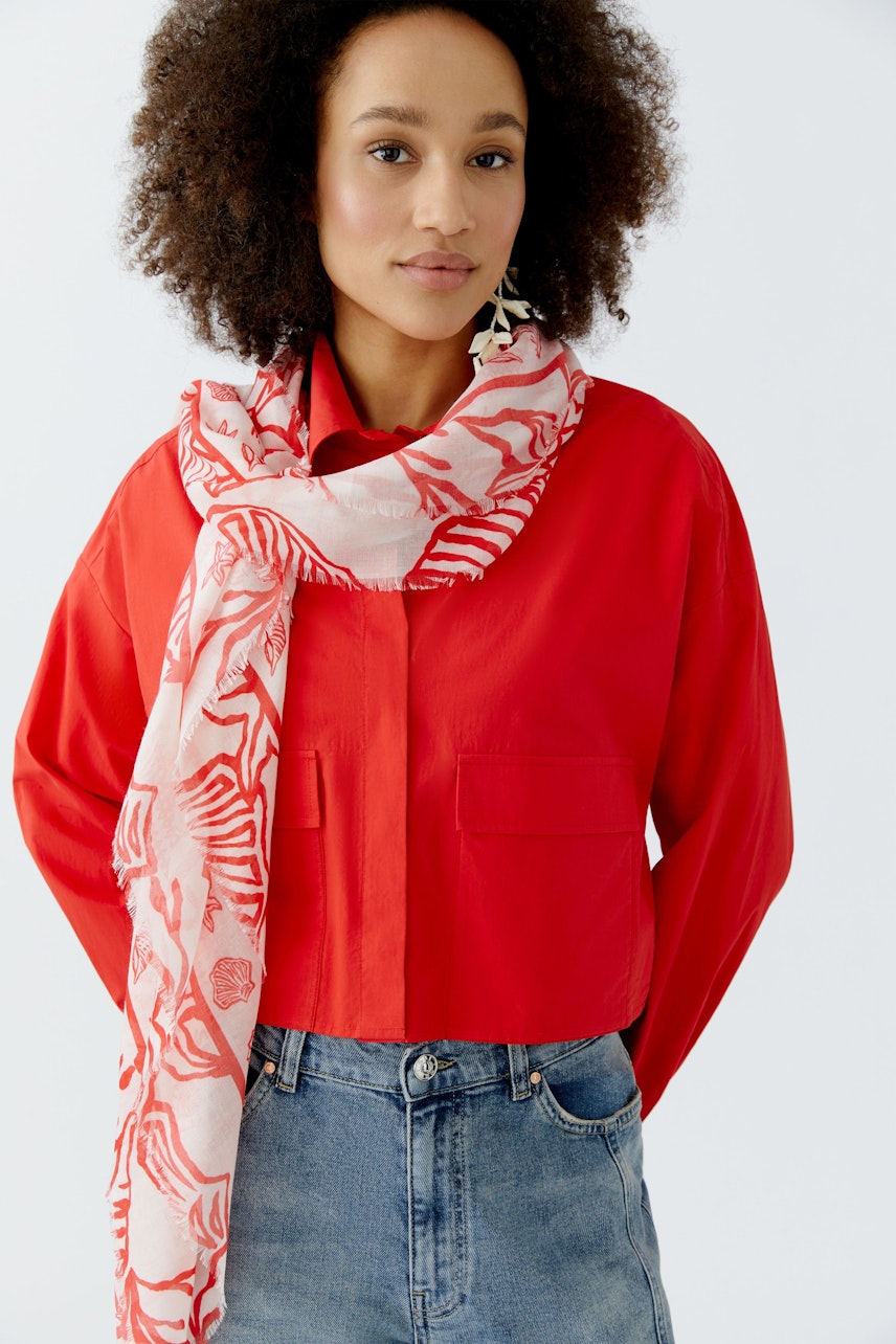 Lightweight scarf: Woman wearing a pink patterned scarf over a red shirt, styled casually.