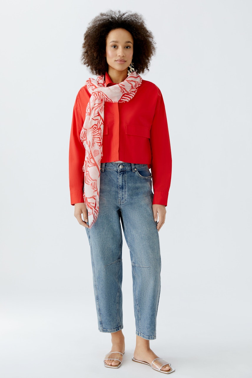 Casual women's scarf: A woman wearing a pink patterned scarf over a red top and blue jeans.