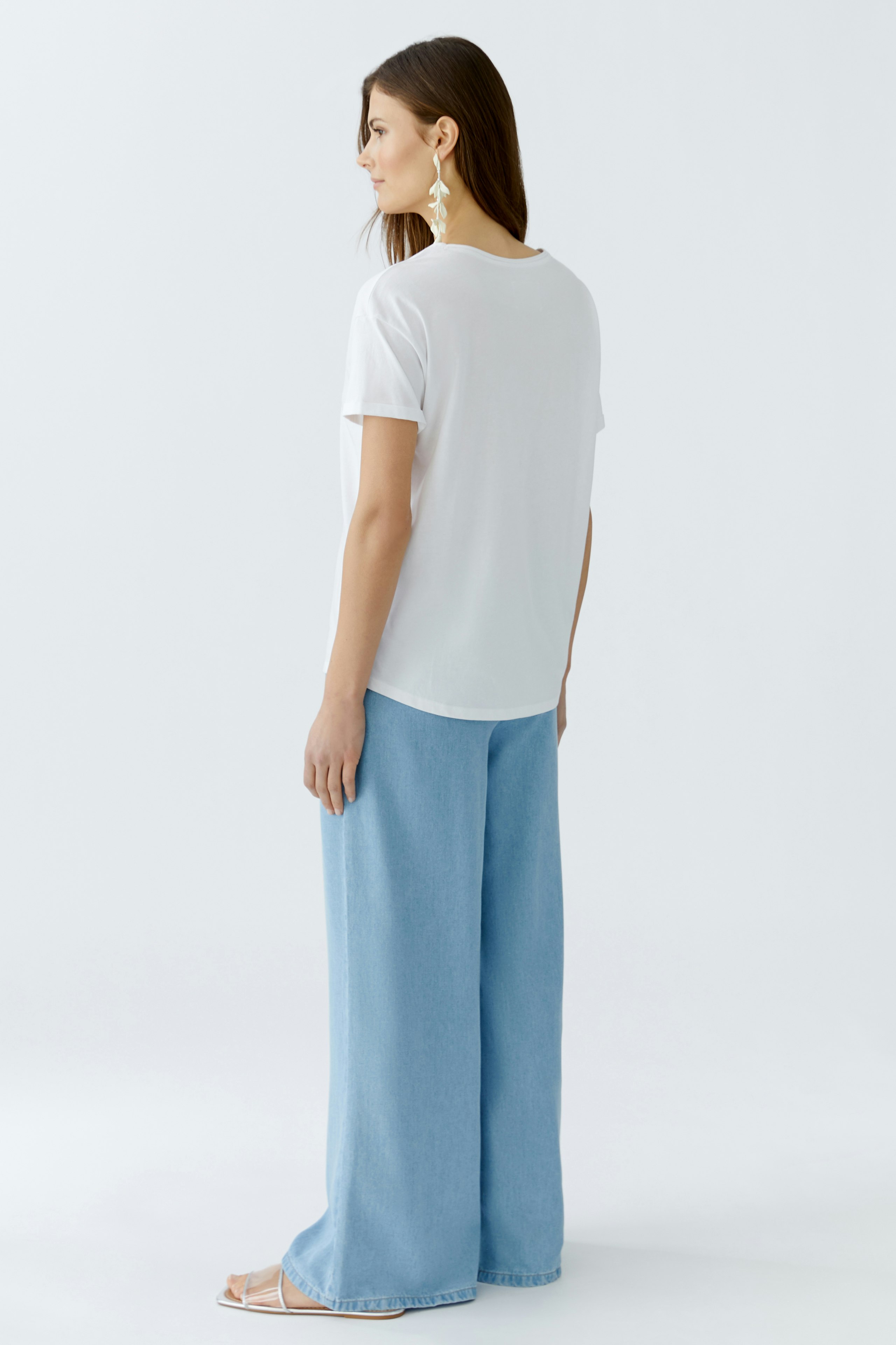 Damen-T-Shirt: Frau in weißem T-Shirt mit lässigem Schnitt und weiten Jeans steht entspannt.