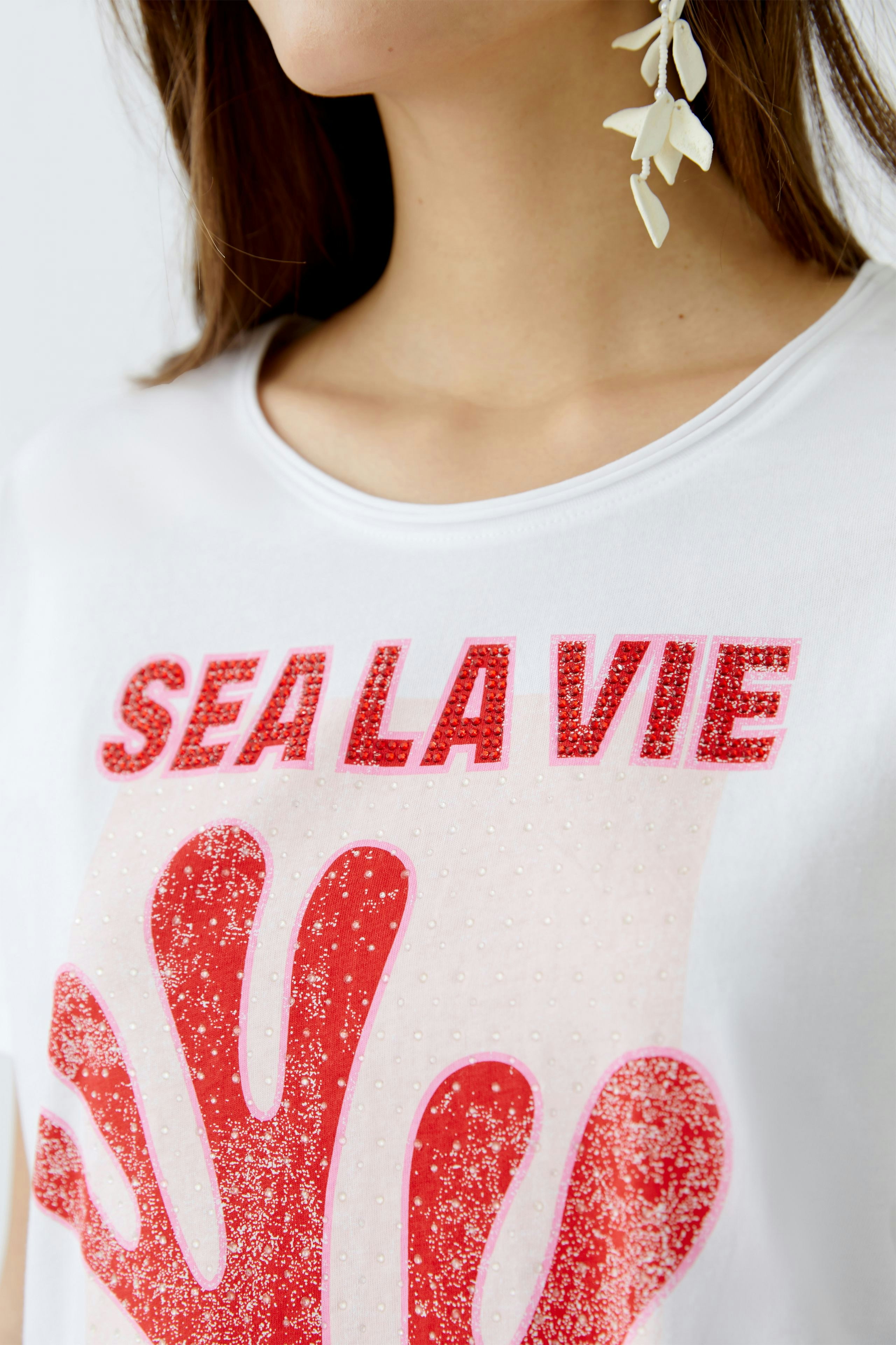 Damen-T-Shirt: Frau trägt ein weißes T-Shirt mit rotem Glitzer-Print und lässigem Rundhalsausschnitt.