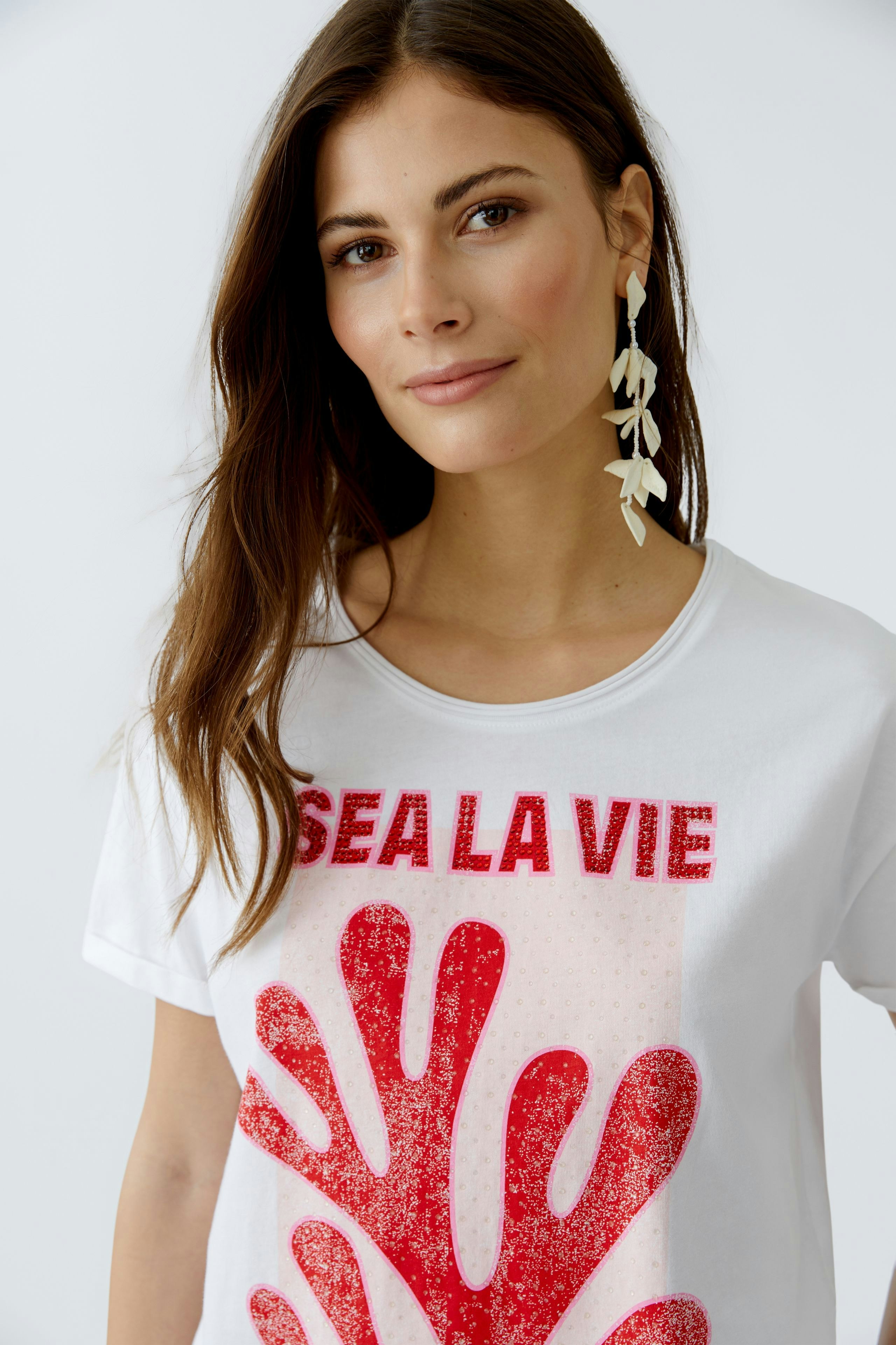 Damen-T-Shirt: Frau trägt ein weißes T-Shirt mit rotem Aufdruck und lässigem Design.
