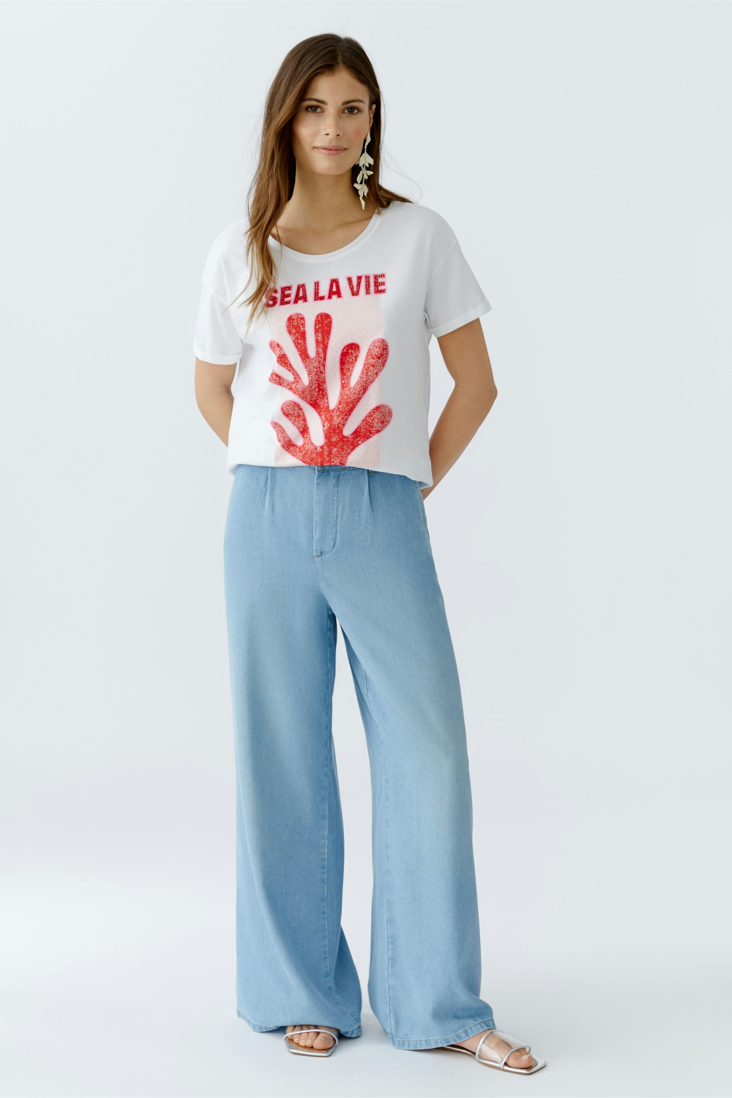 Damen-T-Shirt: Junge Frau trägt ein weißes T-Shirt mit rotem Aufdruck und lässigen Jeans.