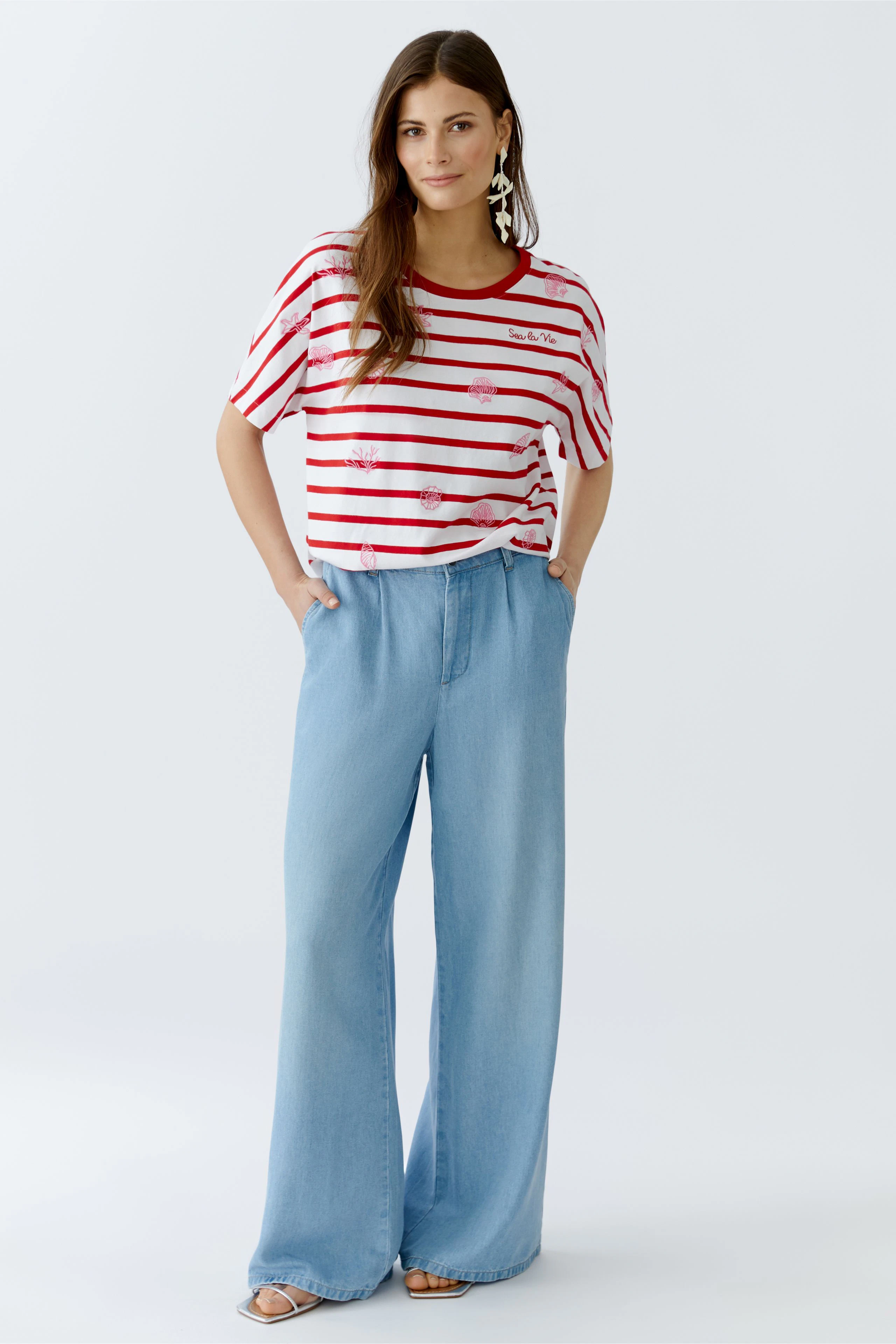 Lässiges Damen-T-Shirt: Frau in gestreiftem Shirt mit roten und weißen Streifen, kombiniert mit weiten Jeans.