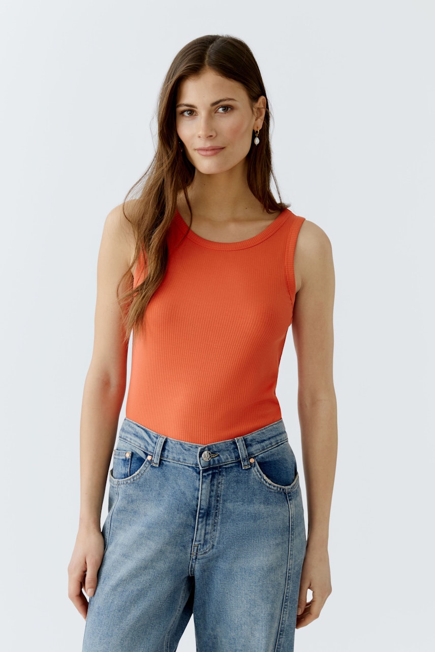 Casual women's top: A woman in a bright orange tank top paired with blue jeans, showcasing a relaxed style.