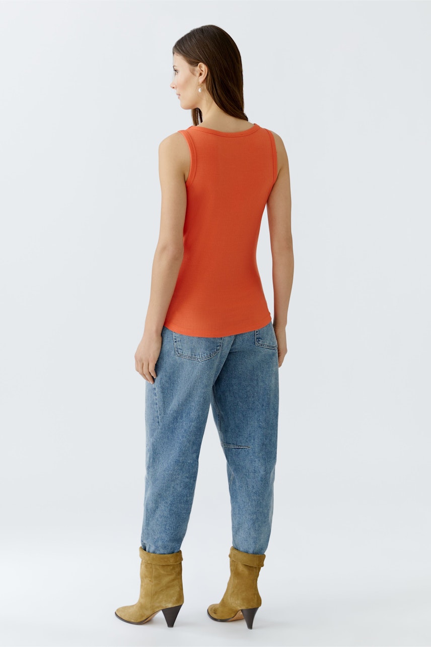 Casual women's top: Young woman in a fitted orange tank top paired with relaxed jeans.