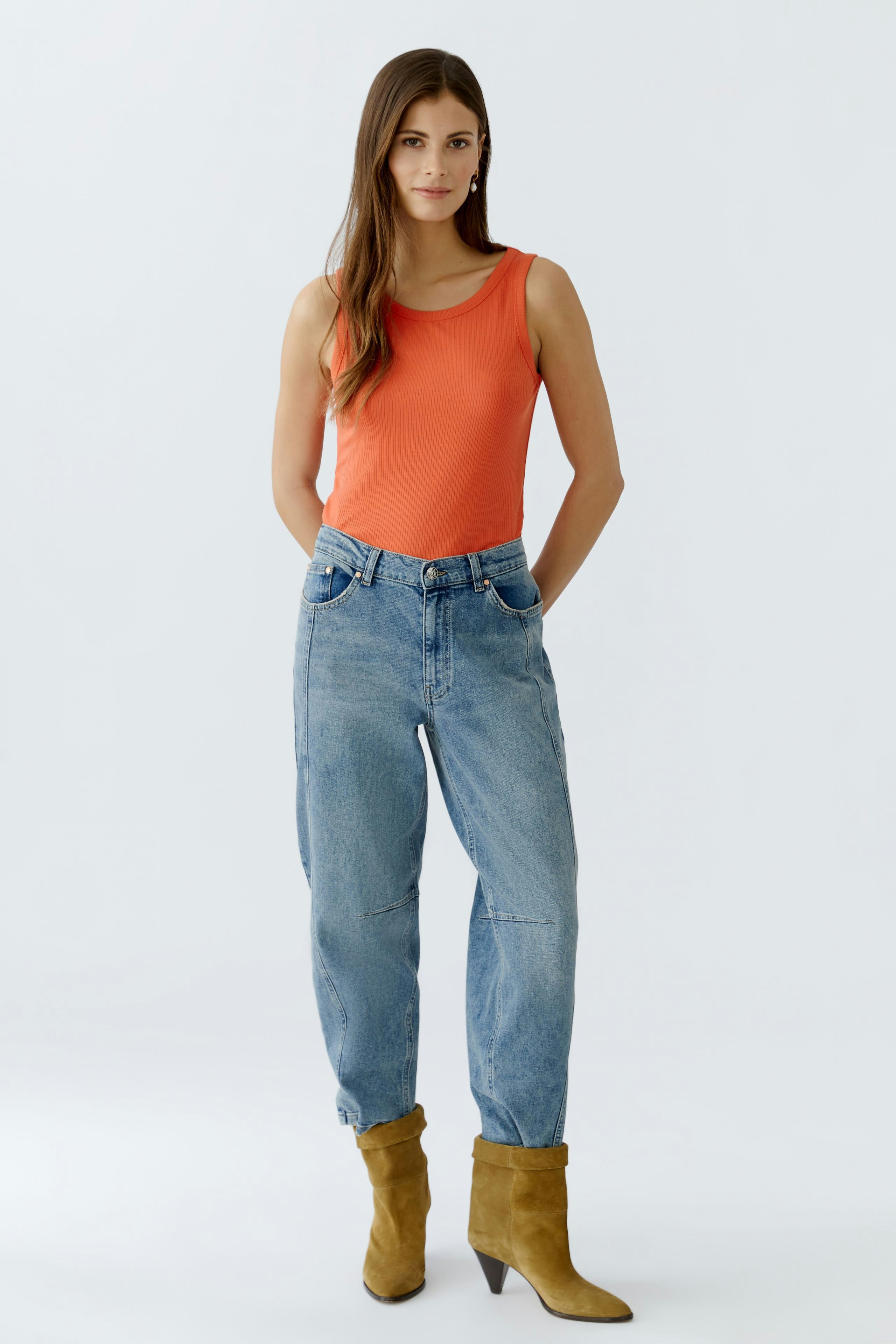 Damen-Top in leuchtendem Orange: Frau trägt ein ärmelloses Oberteil mit lässigen Jeans und Stiefeln.