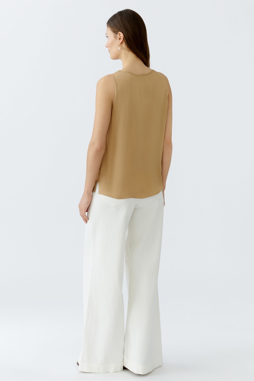 Bequeme Damen-Top: Frau in einem sandfarbenen Top und weißen, weiten Hosen von hinten.