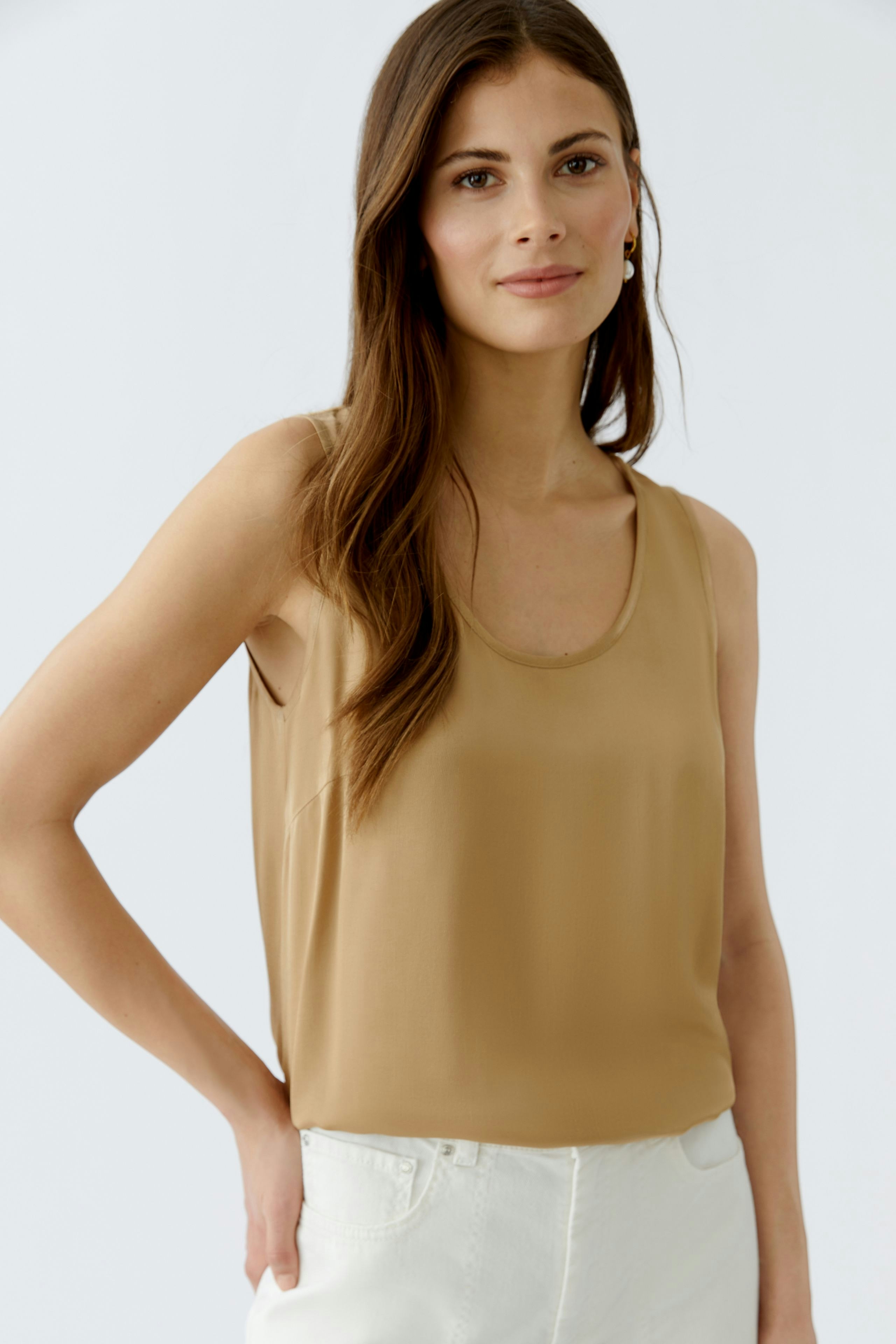 Casual women's top: Young woman in a light brown sleeveless top paired with white pants.