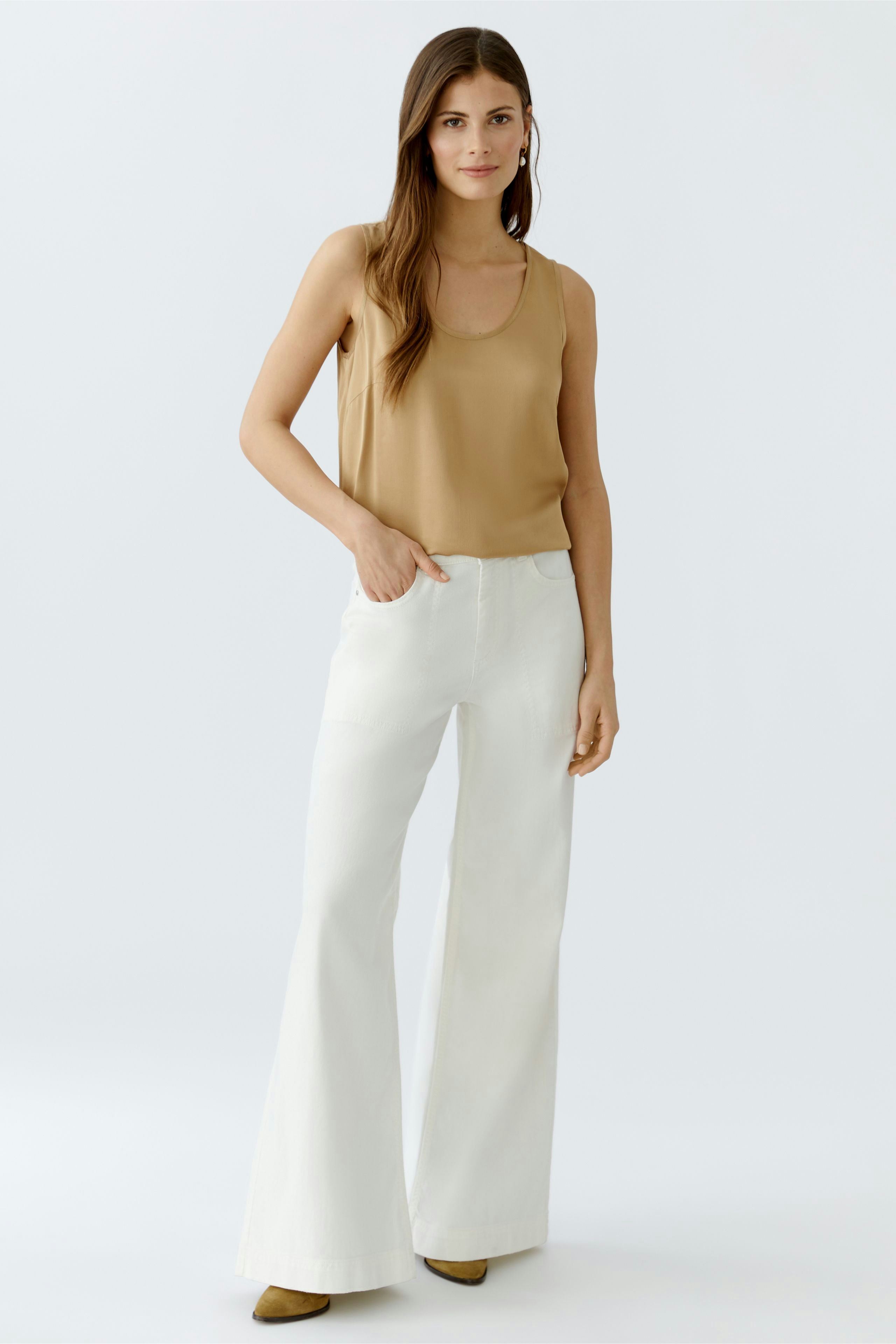 Casual women's top: A woman in a beige tank top paired with white wide-leg pants, looking relaxed.