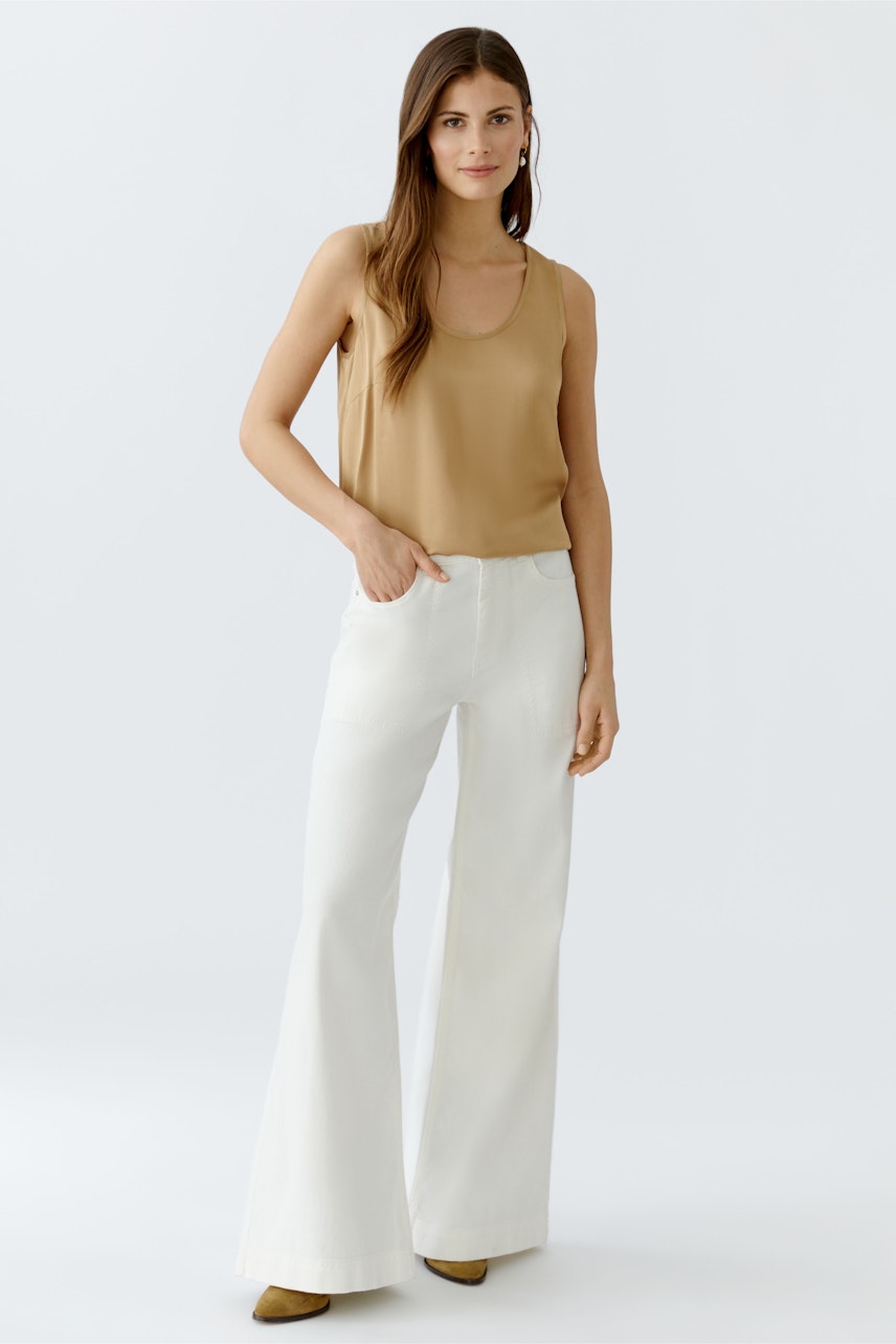 Beige Damen-Top: Frau in einem schlichten, ärmellosen Top mit Rundhalsausschnitt und weißen, weiten Hosen.