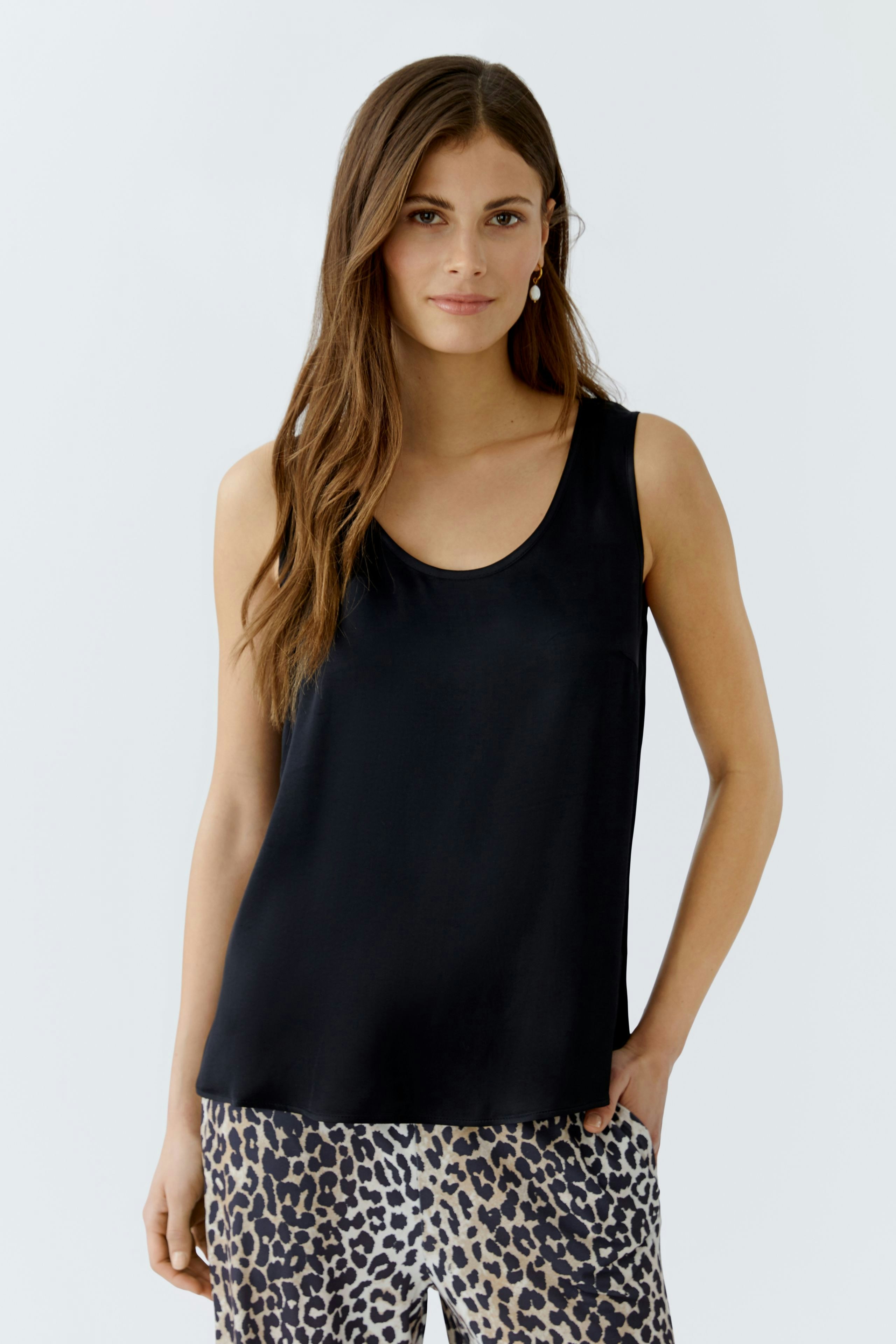 Schwarzes Damen-Top: Junge Frau trägt ein schlichtes, ärmelloses Top und kombiniert es mit einem gemusterten Rock.