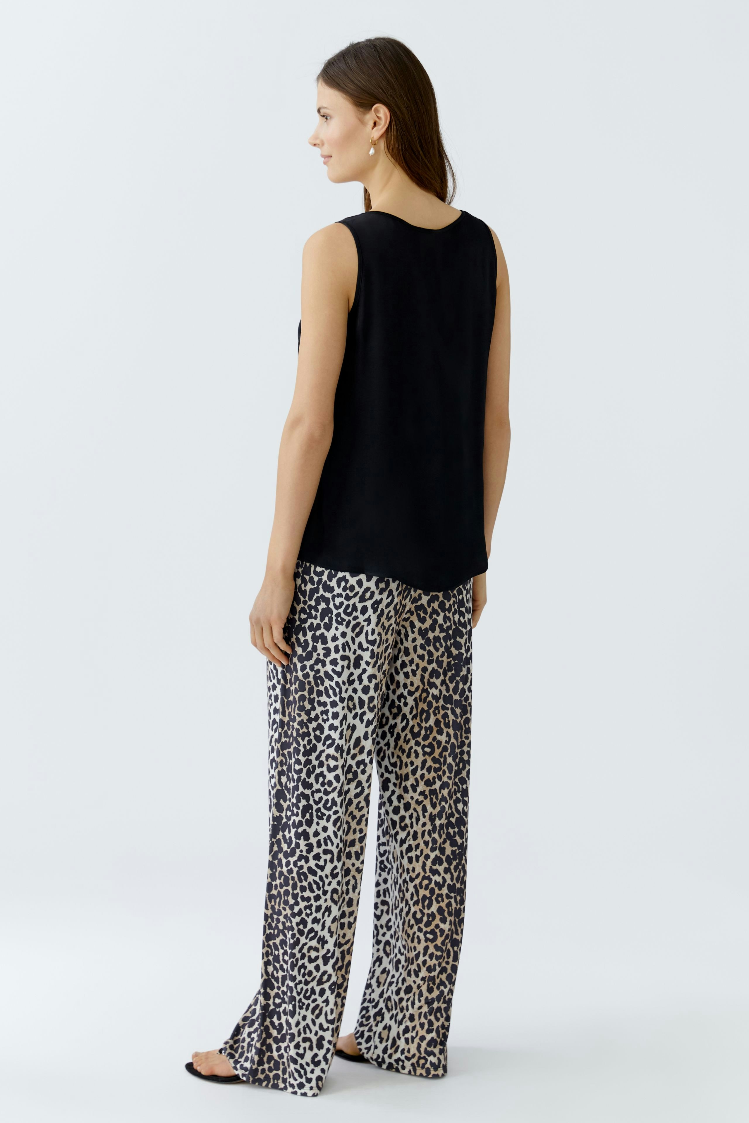 Schwarzes Damen-Top: Frau mit ärmellosem Oberteil und lässigen, gemusterten Hosen von hinten.