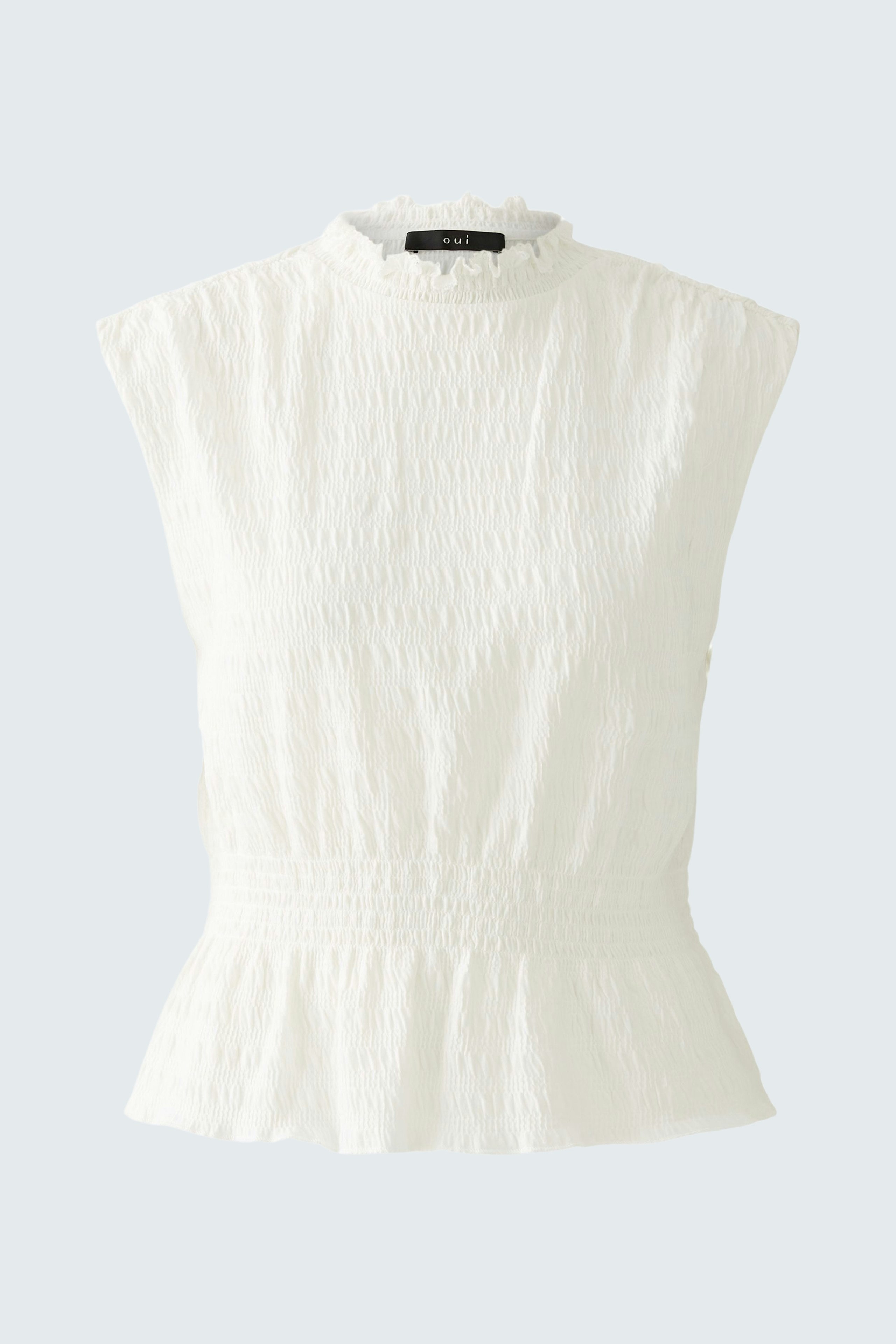 Elegant women's top: A woman in a white, textured top with a ruffled neckline and peplum hem.