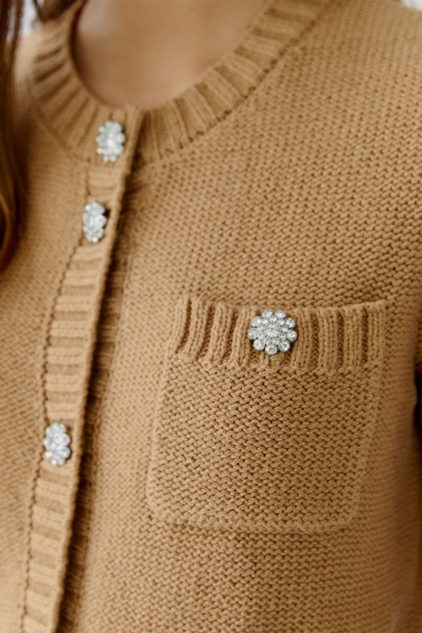 Beige Strickjacke: Frau trägt eine kuschelige Strickjacke mit Schmuckknöpfen und einer Brusttasche.