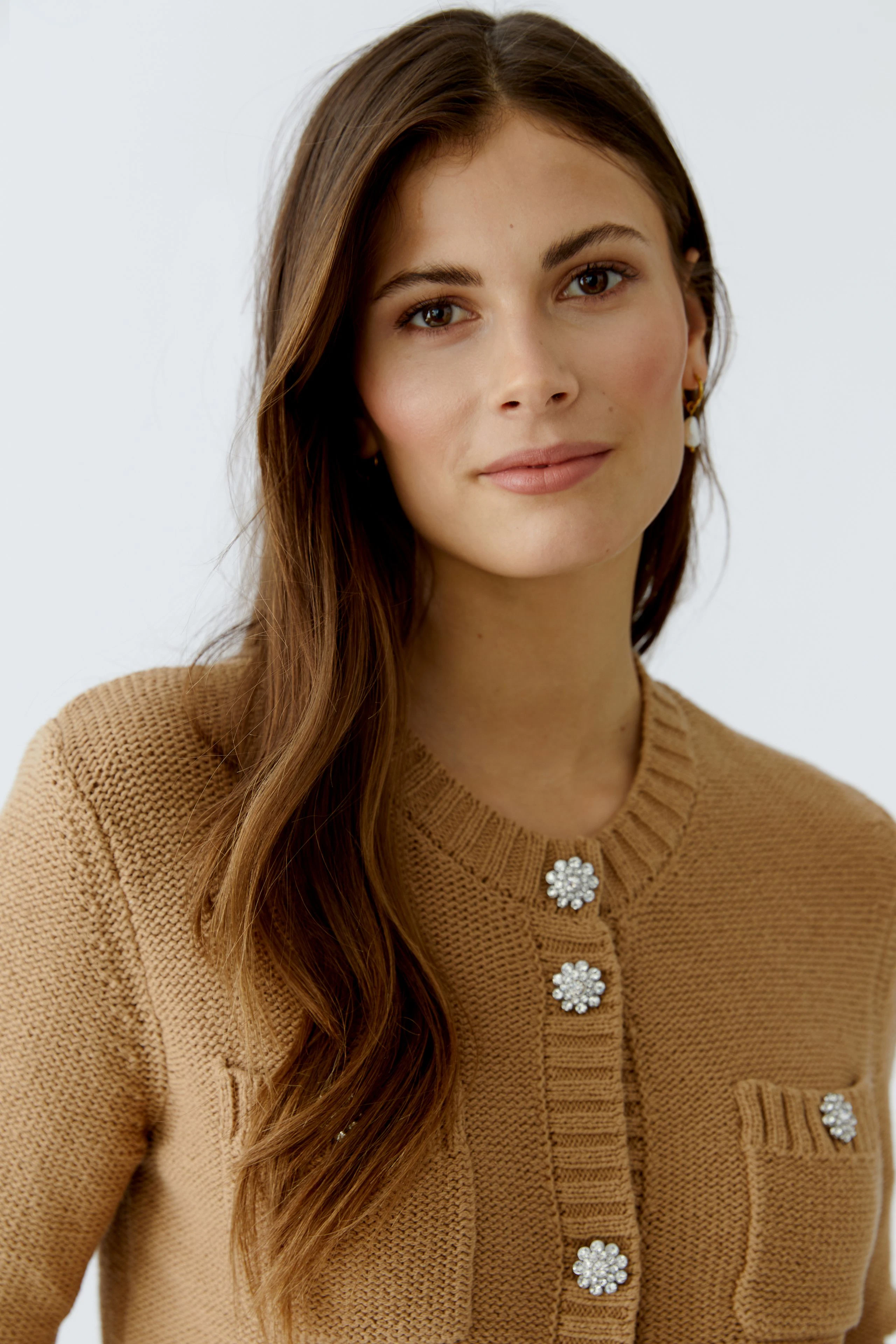 Casual women's cardigan: A woman in a beige knitted cardigan with decorative buttons and a pocket.