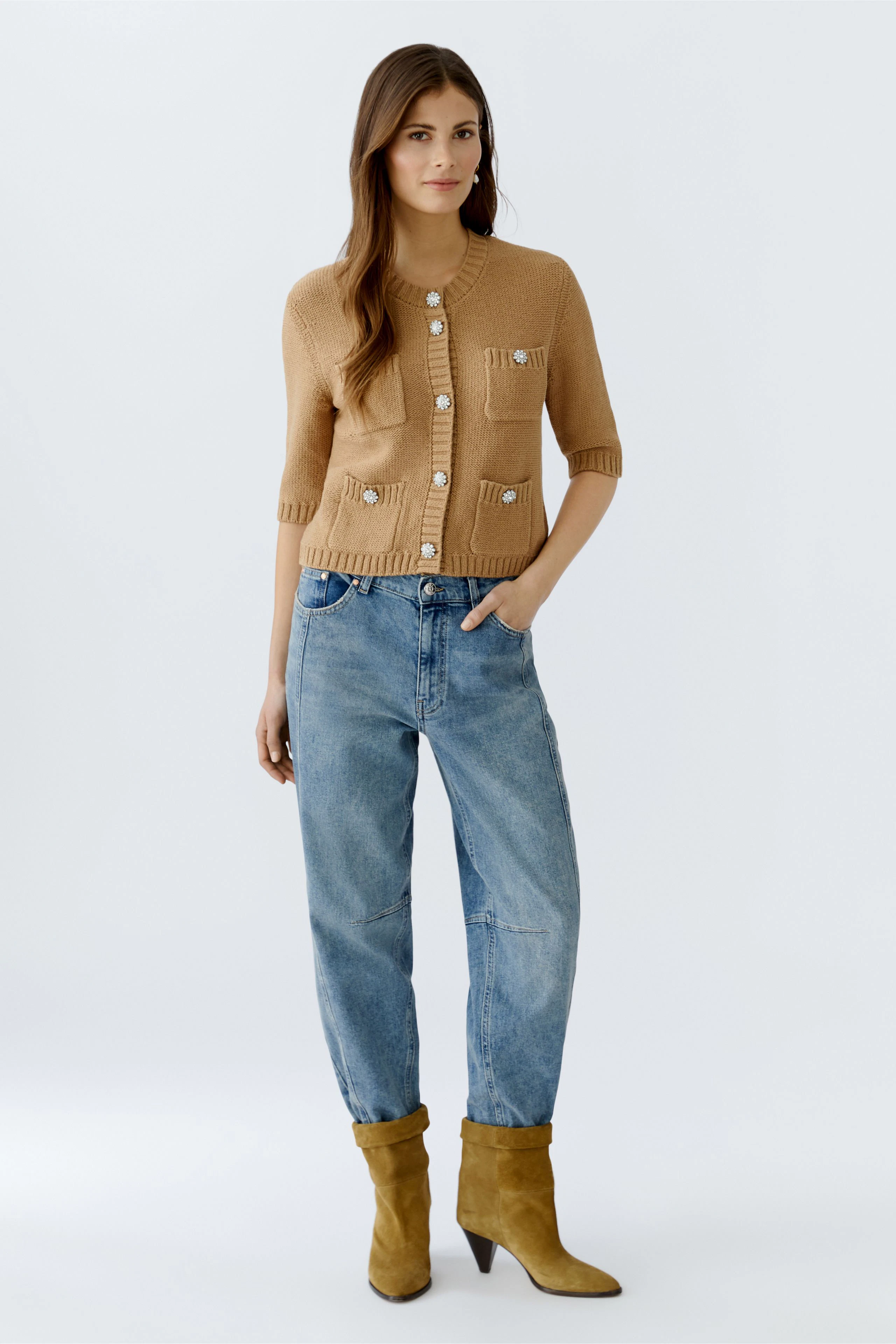 Casual women's cardigan: A woman in a light brown cardigan with buttons and relaxed jeans stands confidently.