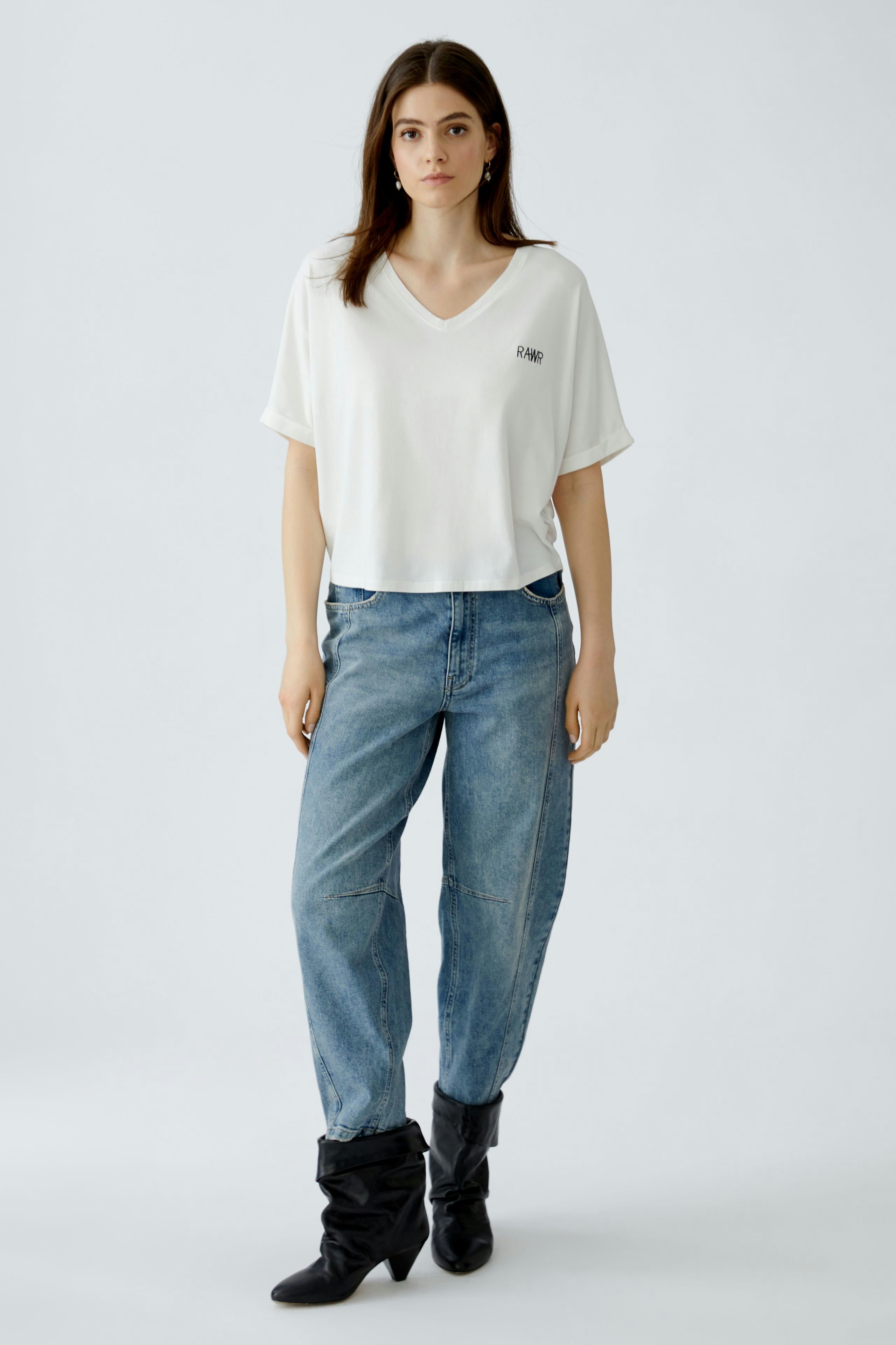 Bequeme Damen-T-Shirt: Frau in weißem V-Ausschnitt-Shirt mit lässigen Jeans und modischen Stiefeln.