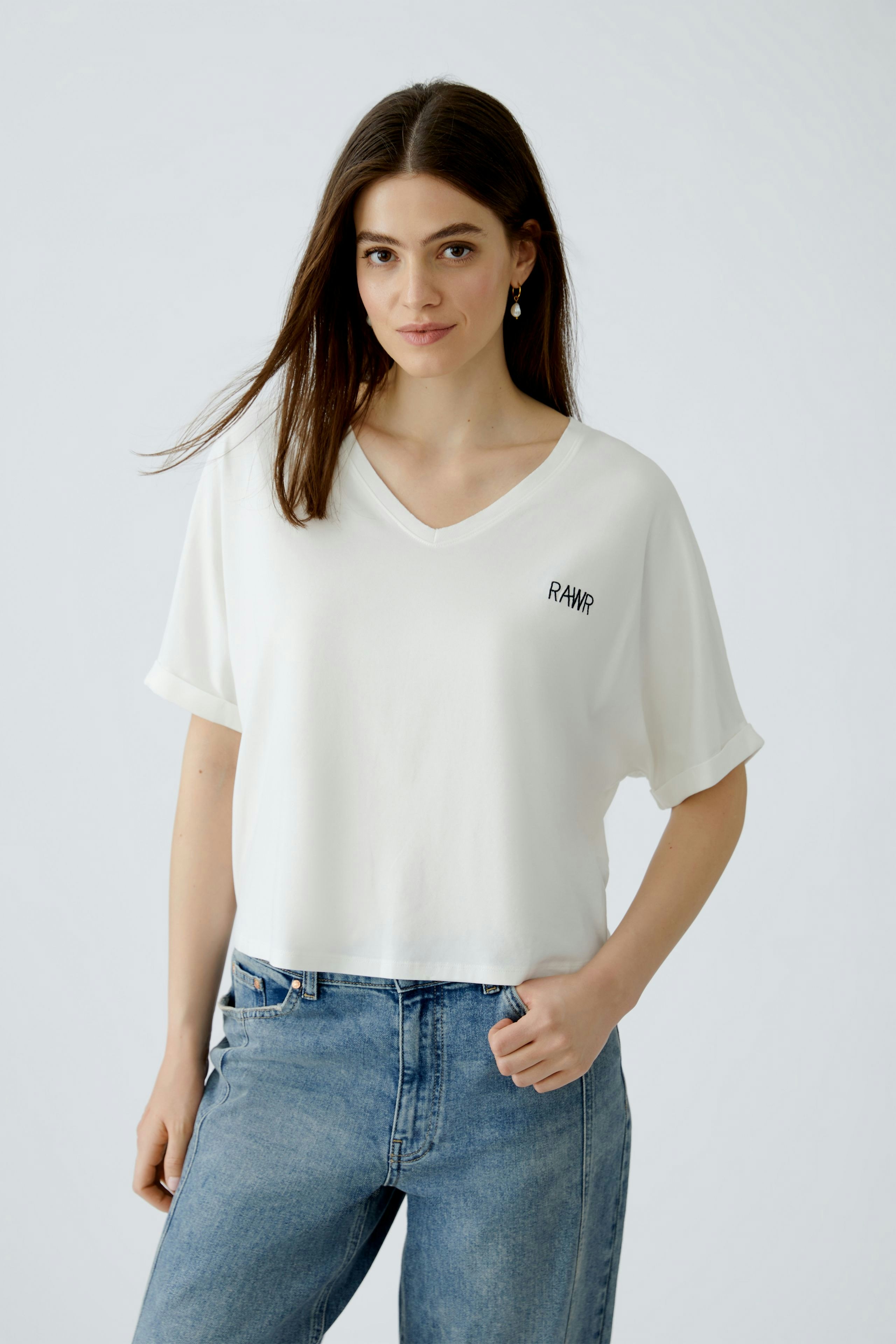 Lässiges Damen-T-Shirt: Frau trägt ein weißes, lockeres T-Shirt mit V-Ausschnitt und lässigen Jeans.