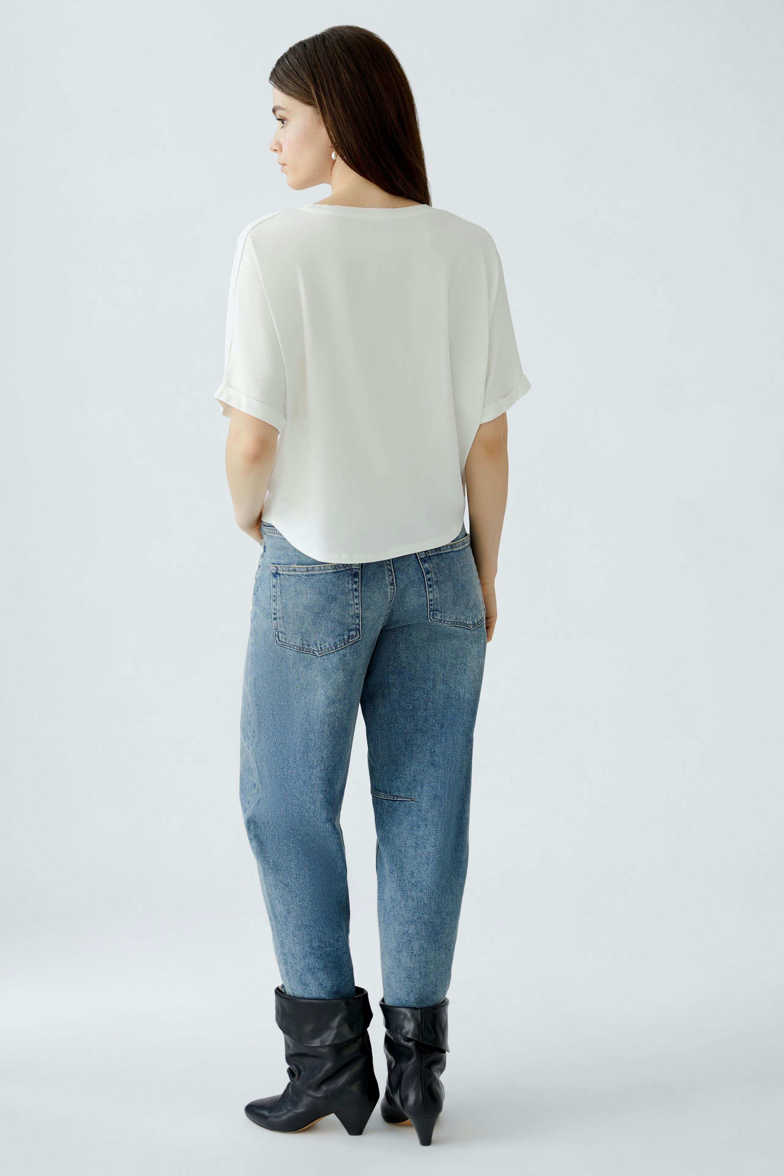 Damen-T-Shirt: Frau in weißem, lässigem T-Shirt und Jeans mit Stiefeln von hinten.