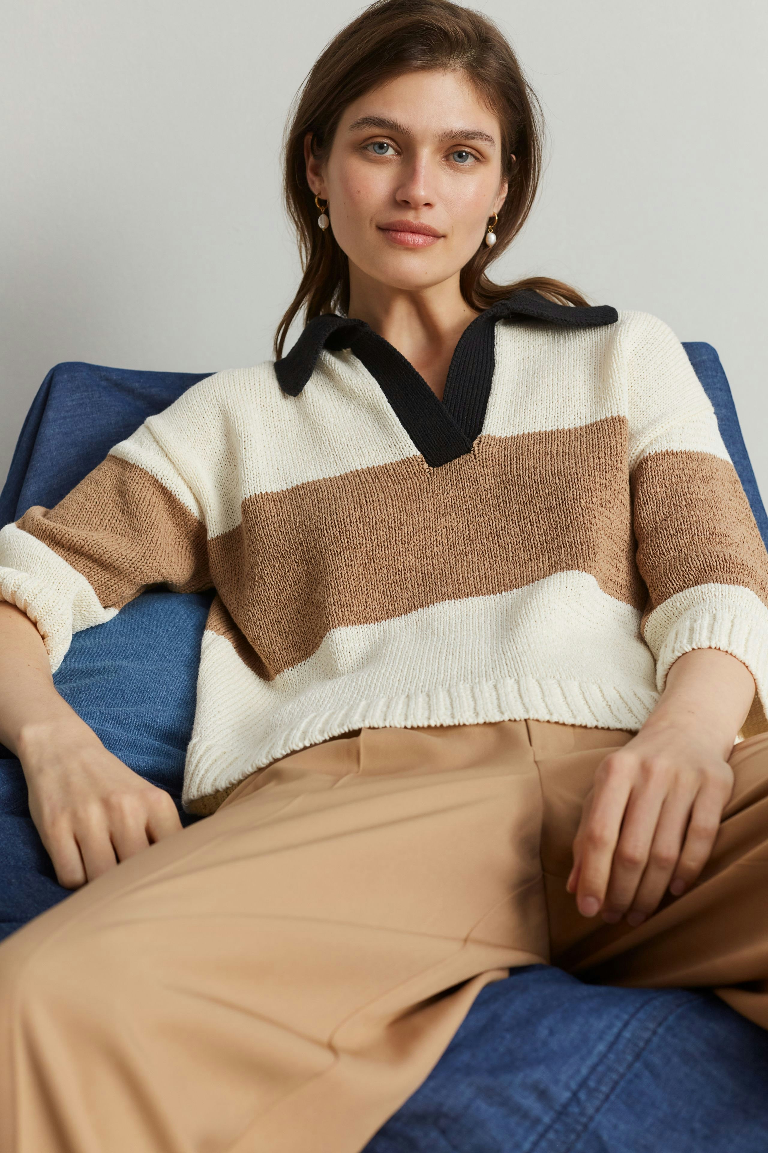 Casual women's pullover: Young woman in a striped pullover with a black collar, relaxed on a blue couch.