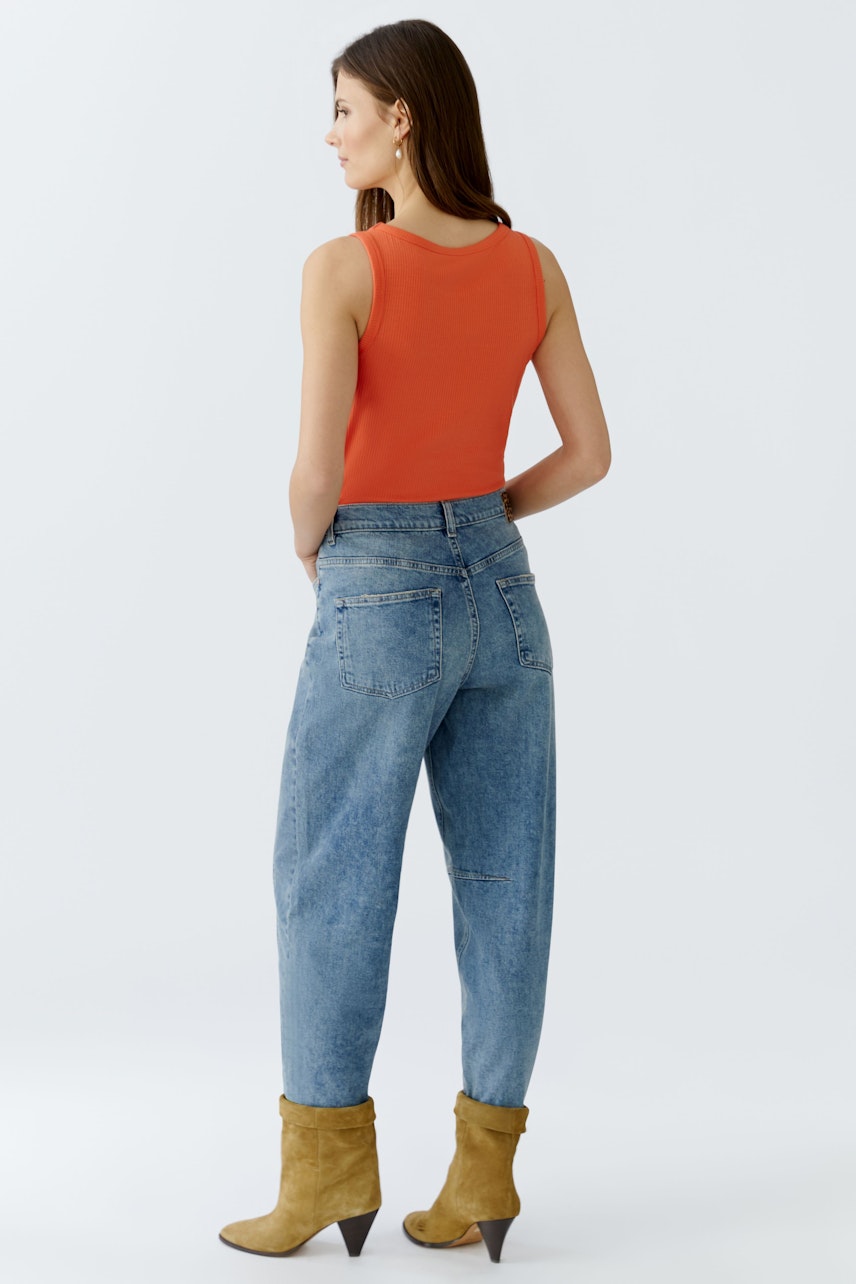 Casual women's jeans: A woman in blue barrel jeans and a white tank top stands with her back to the camera.