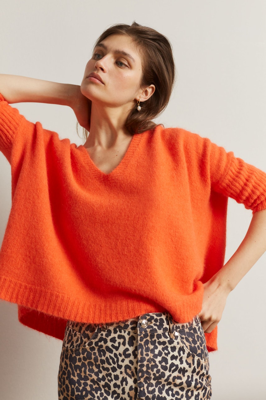 Damen-Jeansrock: Frau in orangefarbenem Pullover und Jeansrock mit Leopardenmuster posiert selbstbewusst.