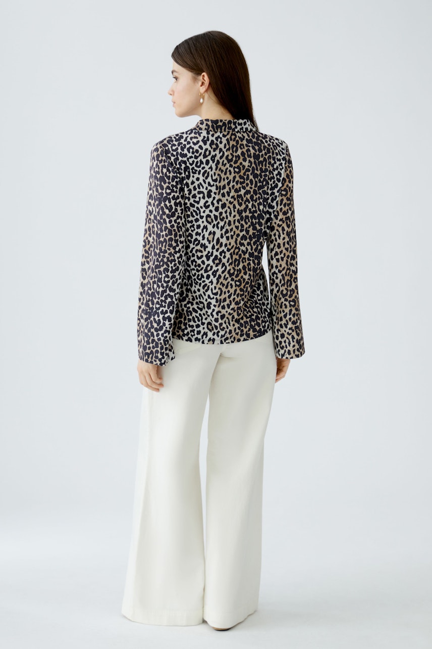 Damen-Bluse im Leo-Design: Frau trägt die Bluse mit langen Ärmeln und lässigen, weißen Hosen.