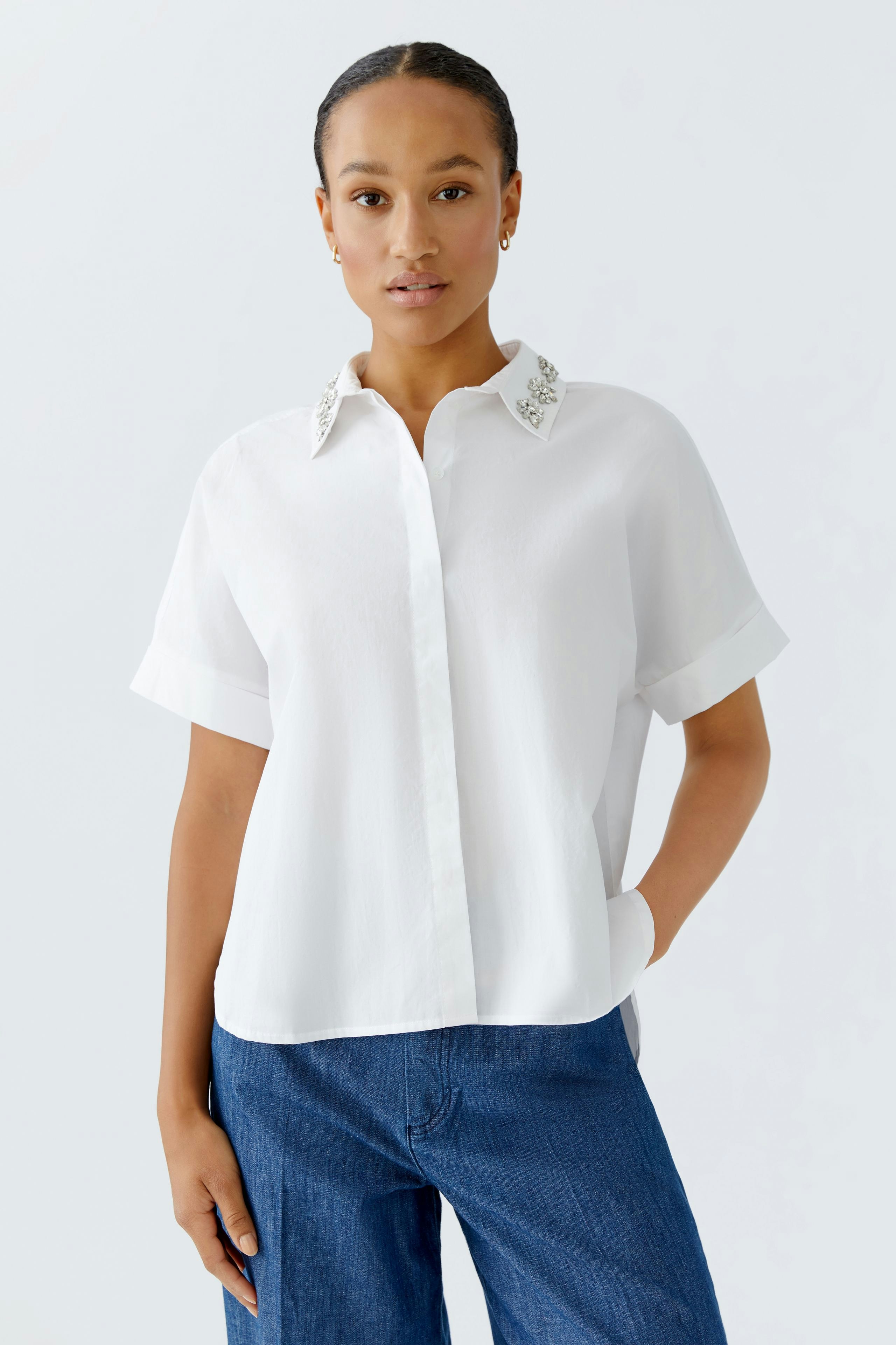 Moderne Damen-Bluse: Frau in weißer Bluse mit besticktem Kragen und lässigen Jeans.