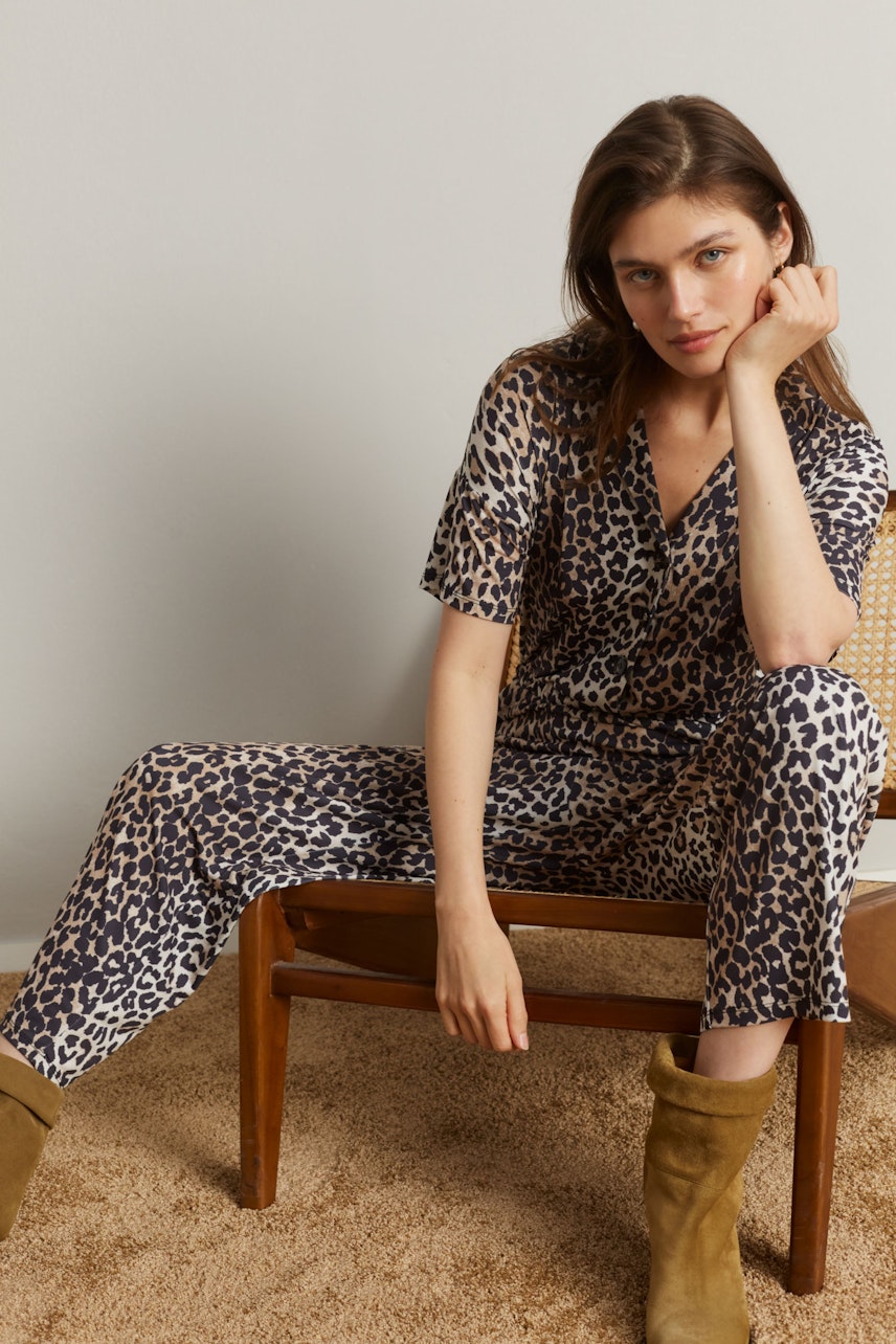 Damen-Jumpsuit im Leo-Design: Frau sitzt entspannt auf einem Stuhl und trägt einen modischen Jumpsuit.
