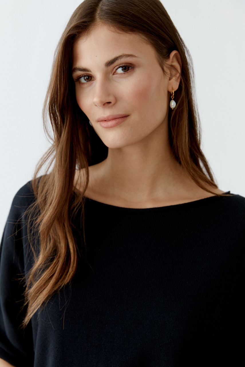 Damen-Pullover: Junge Frau trägt einen lässigen schwarzen Pullover mit weitem Ausschnitt und natürlichem Look.