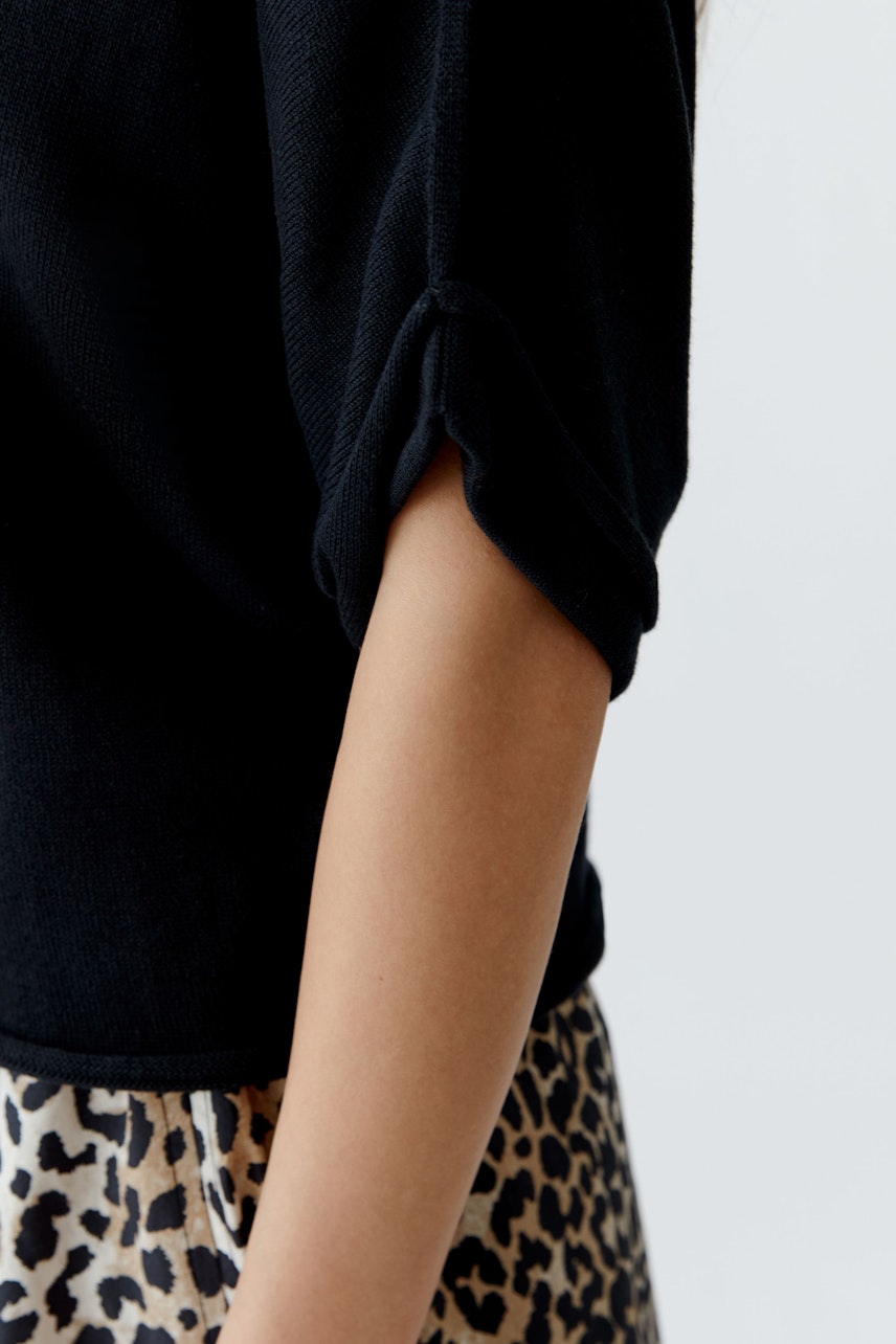 Damen-Pullover: Detailansicht eines schwarzen Pullovers mit lässigen, umgeschlagenen Ärmeln.