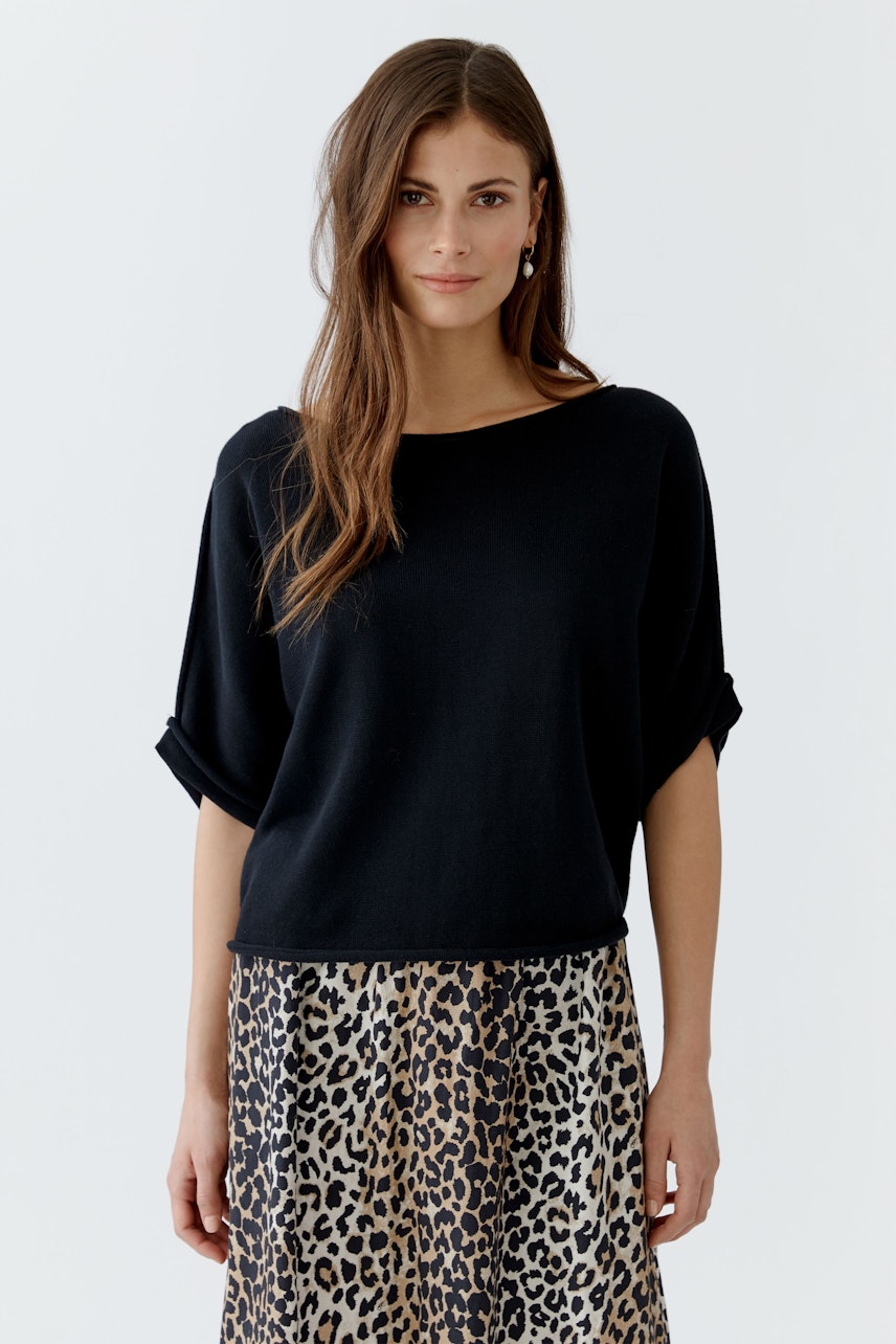 Schwarzer Damen-Pullover mit lässigem Schnitt, kombiniert mit einem gemusterten Rock.
