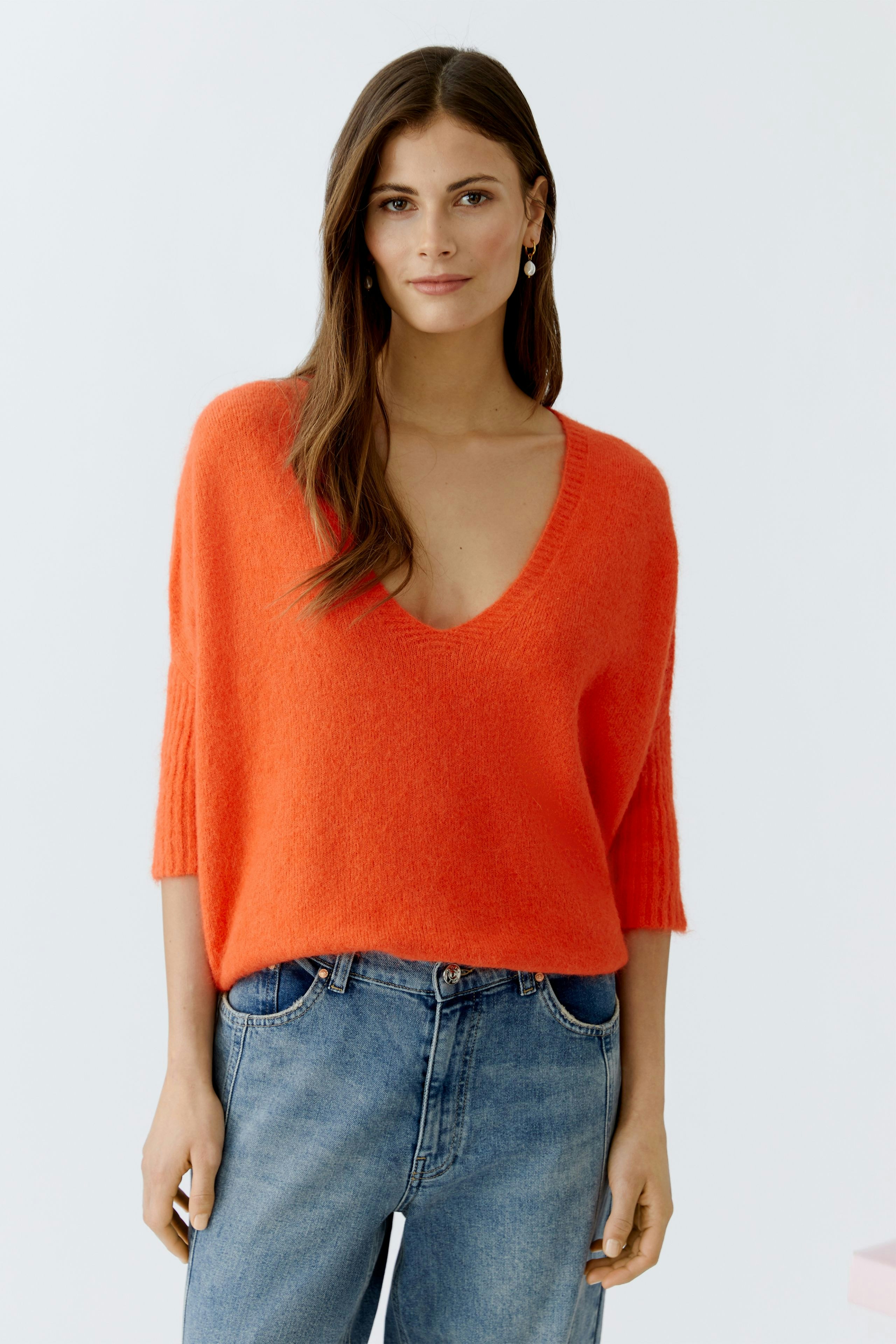 Casual women's pullover: A woman in a vibrant orange pullover with a deep V-neck and relaxed fit.